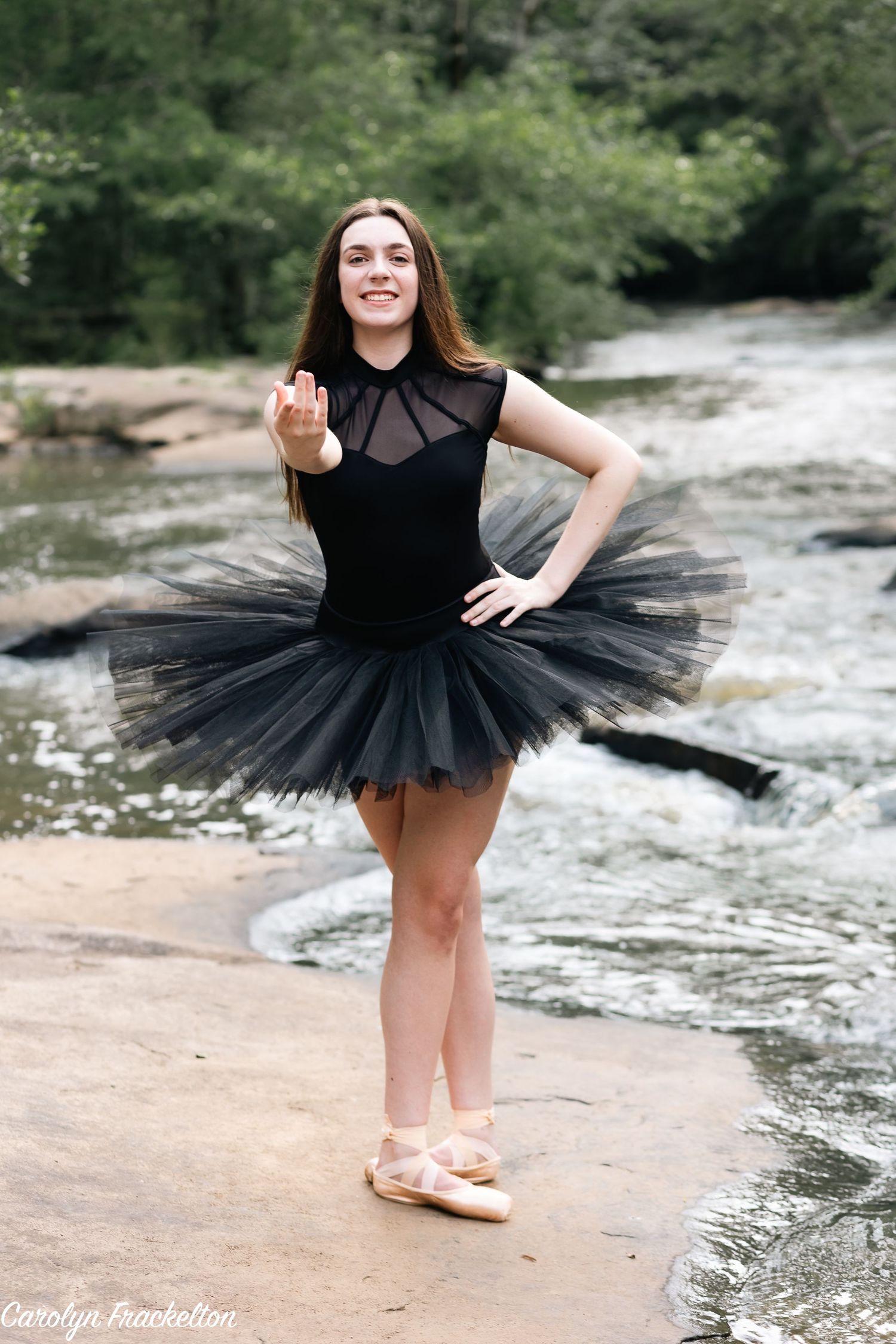 Ballet dancer in black tutu performs elegant poses by a flowing river.