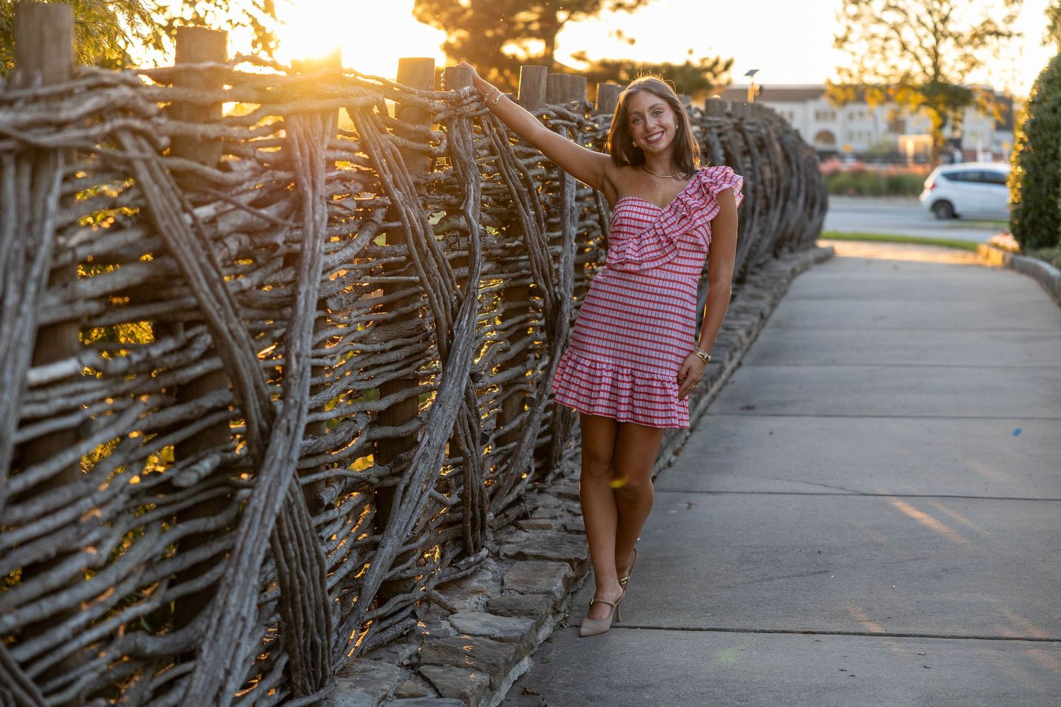A sun flare illuminates a wooden fence and sidewalk during golden hour at sunset.