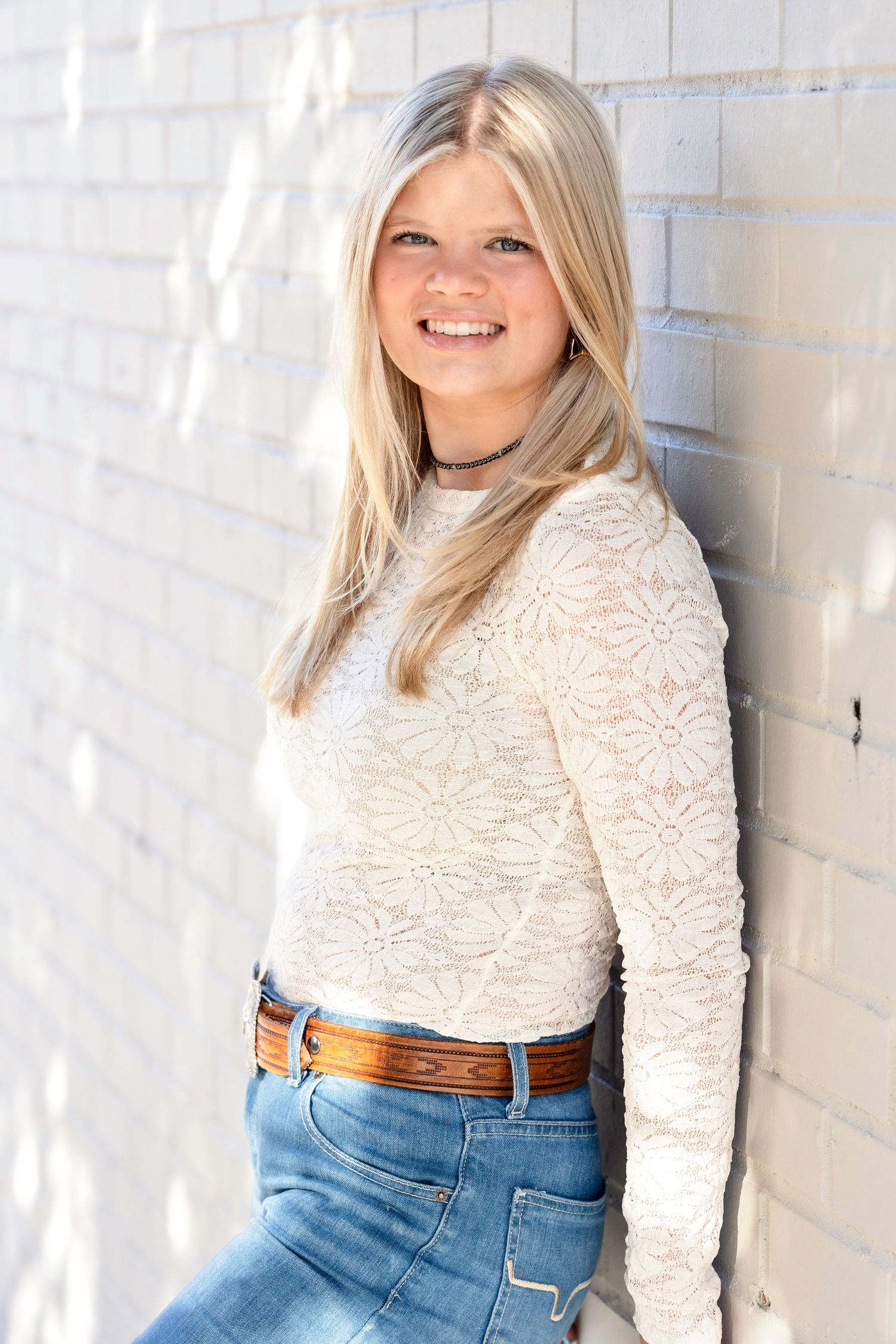 Portrait series against white wall featuring lace top and denim style.