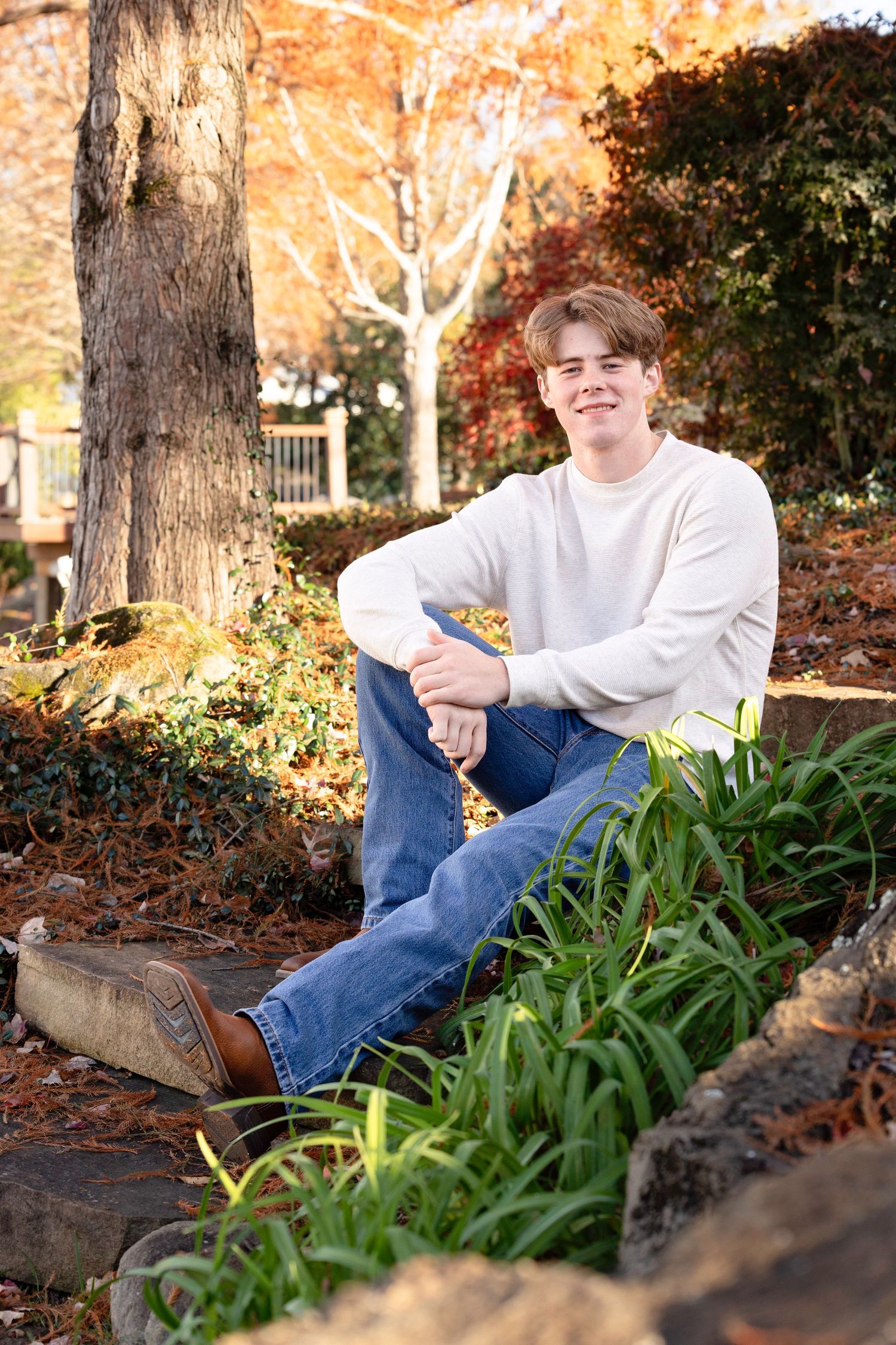 Person reclining on ground with autumn foliage and trees in background wearing casual attire.
