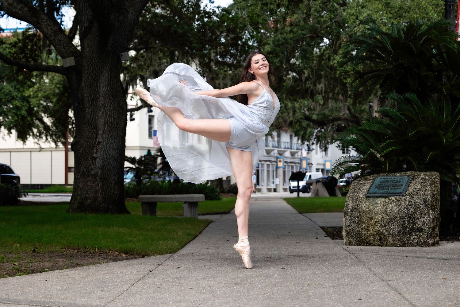 Dancer performs graceful movements outdoors in an urban park setting.