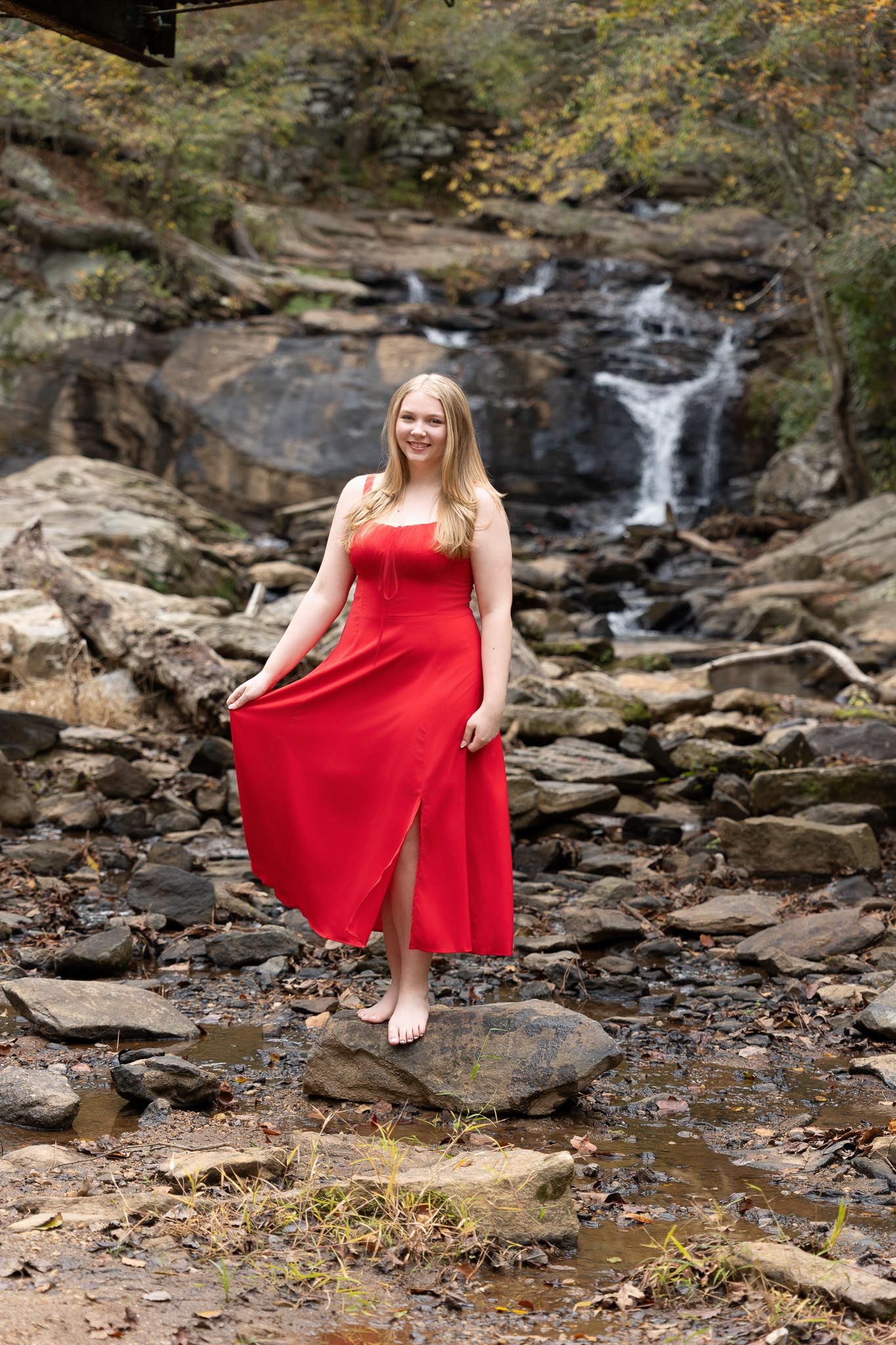 A red dress contrasts beautifully against rocky terrain near a cascading waterfall in a natural outdoor setting.