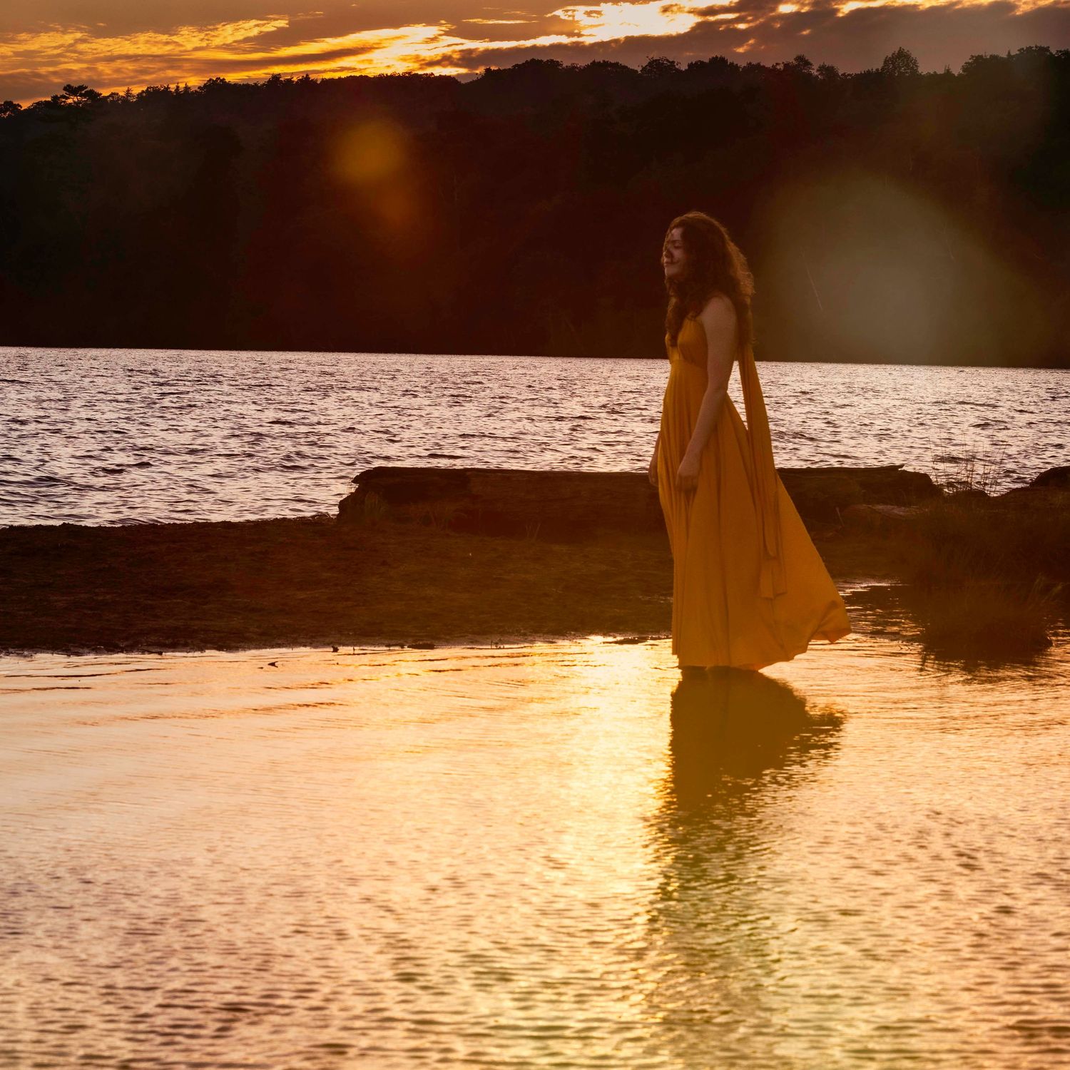 Ethereal sunset scene at a lake with silhouettes reflected in golden water.