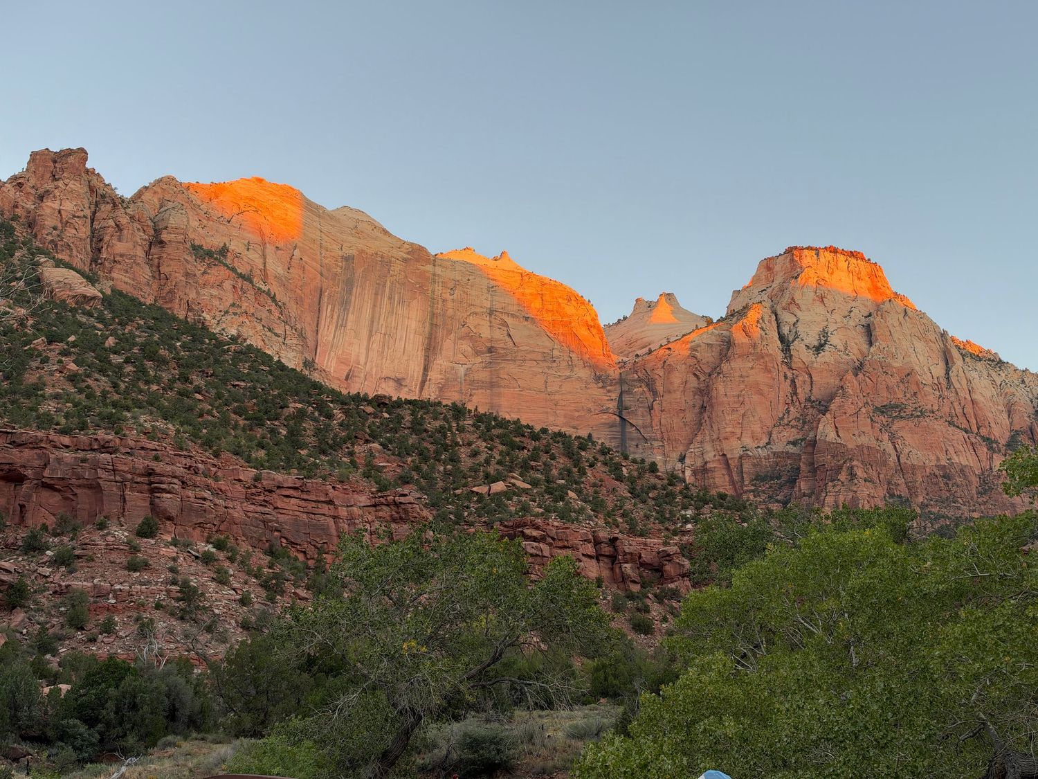 Zion National Park red rock canyon cliffs glowing orange at sunset with green trees in foreground.