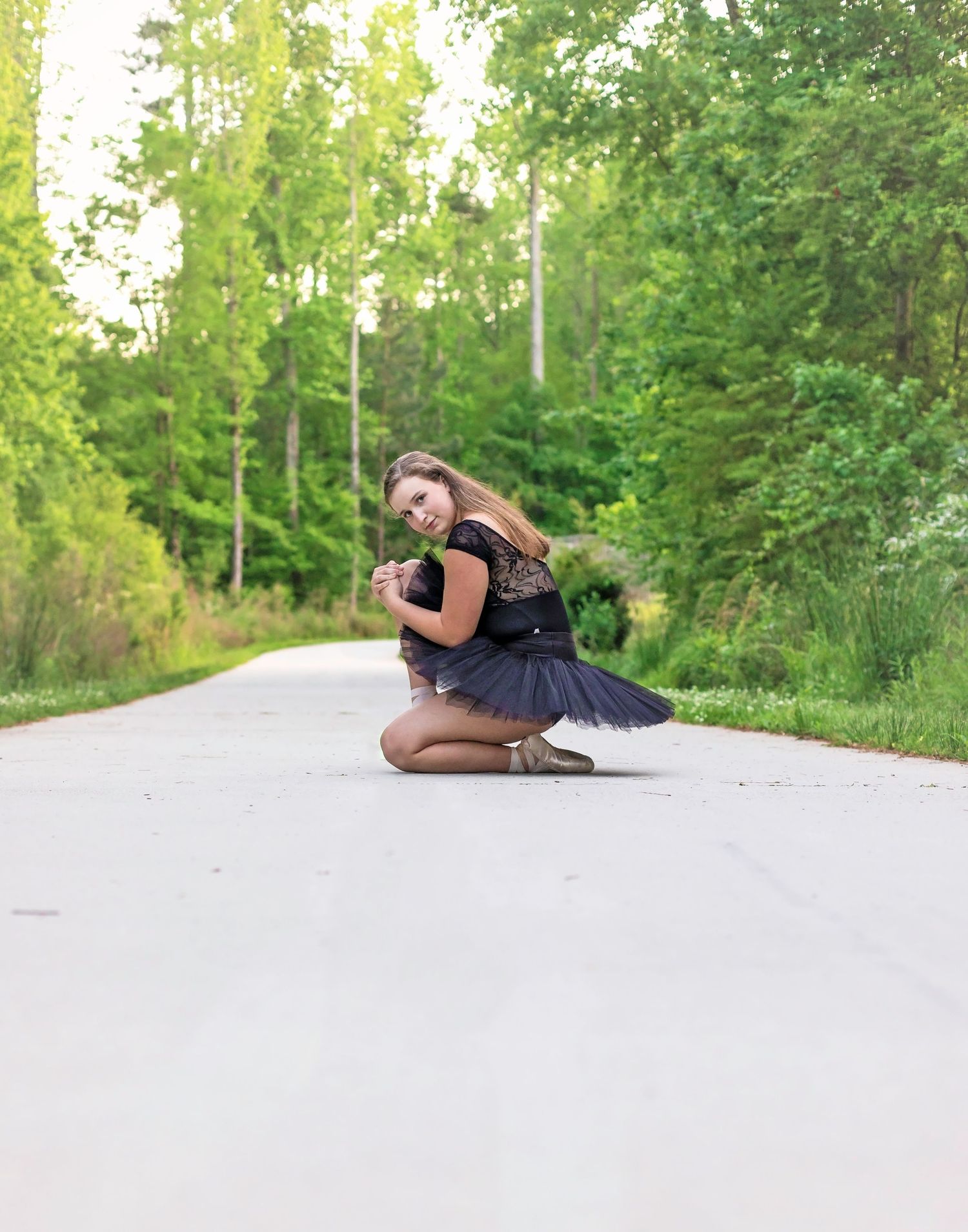 Dancer in black outfit creates artistic poses on white pathway in nature setting.
