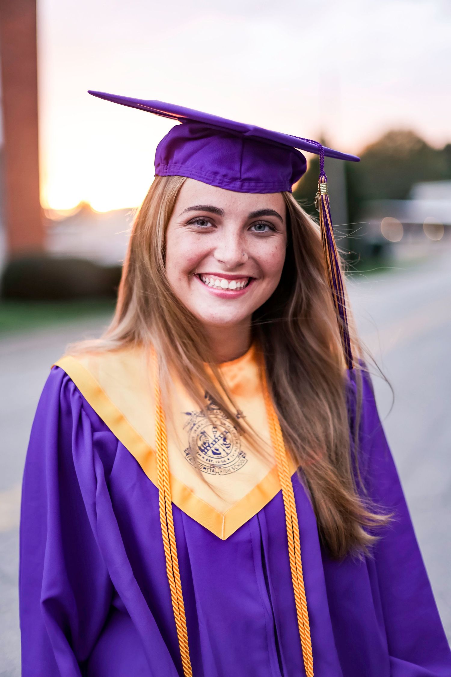 Graduate wearing purple and gold regalia poses for photos outdoors.