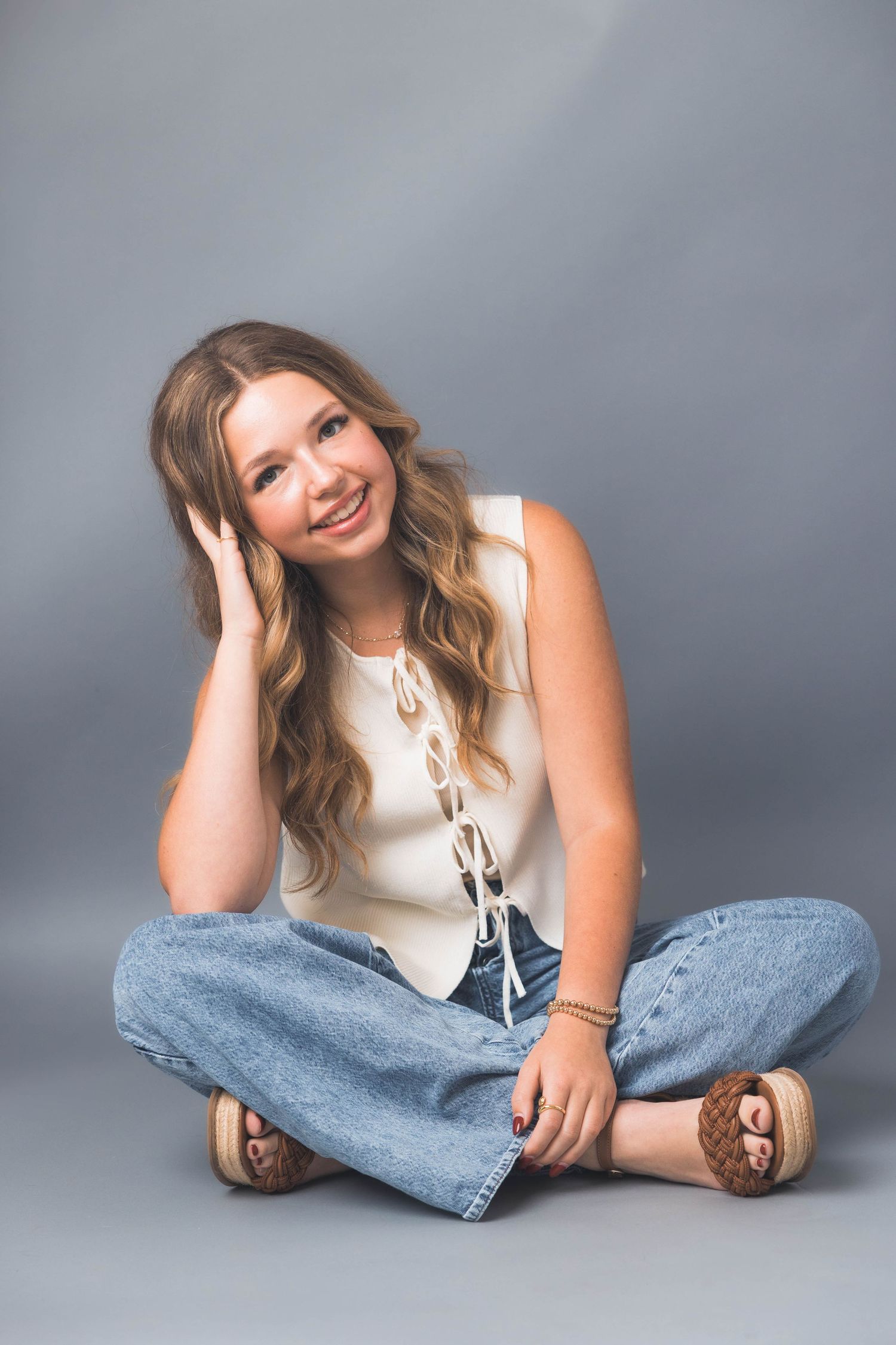 Casual portrait session showing relaxed poses in white top and blue jeans on grey backdrop.