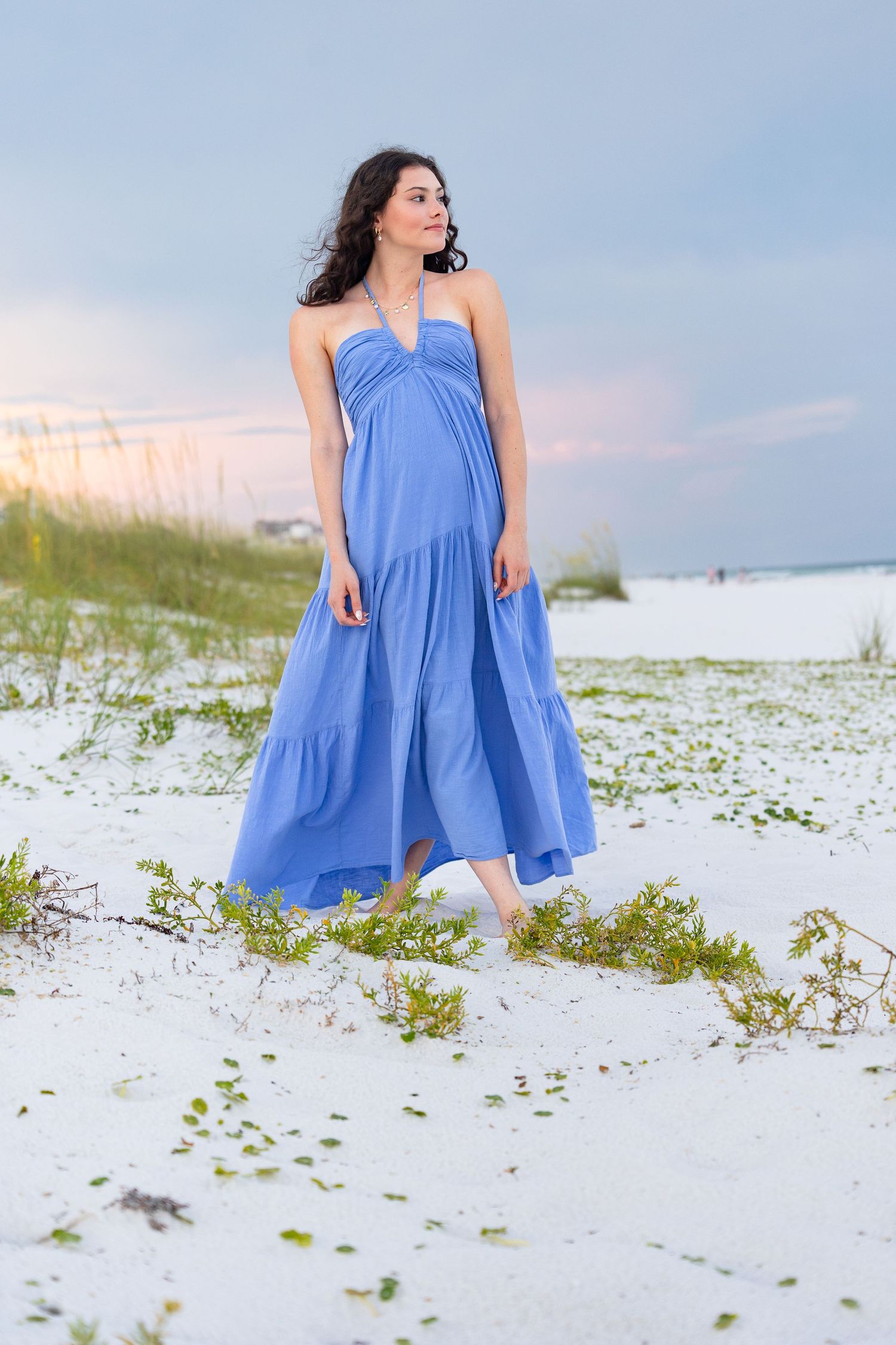 A person in a flowing blue sundress poses gracefully on pristine white sand beach during a serene photoshoot.