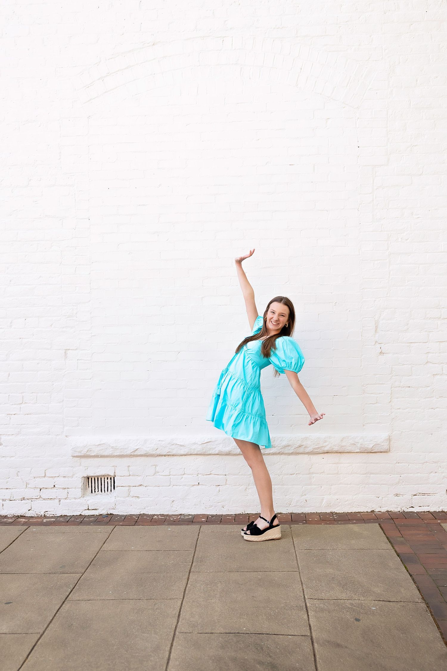 A sequence of photos showing someone in a turquoise dress performing a cartwheel against a white brick wall.