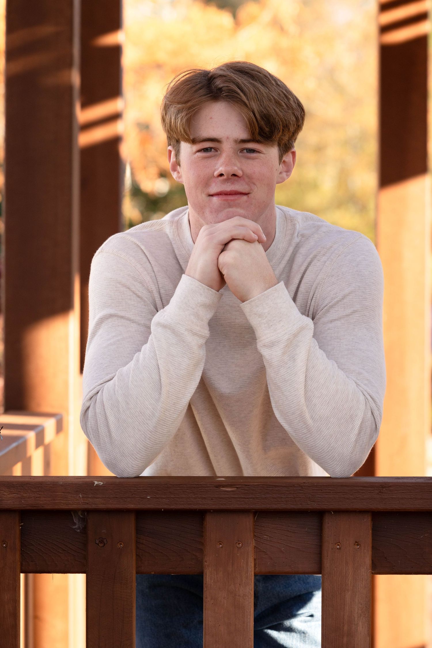 Person in gray sweater rests head on hands while leaning on wooden railing in warm lighting.
