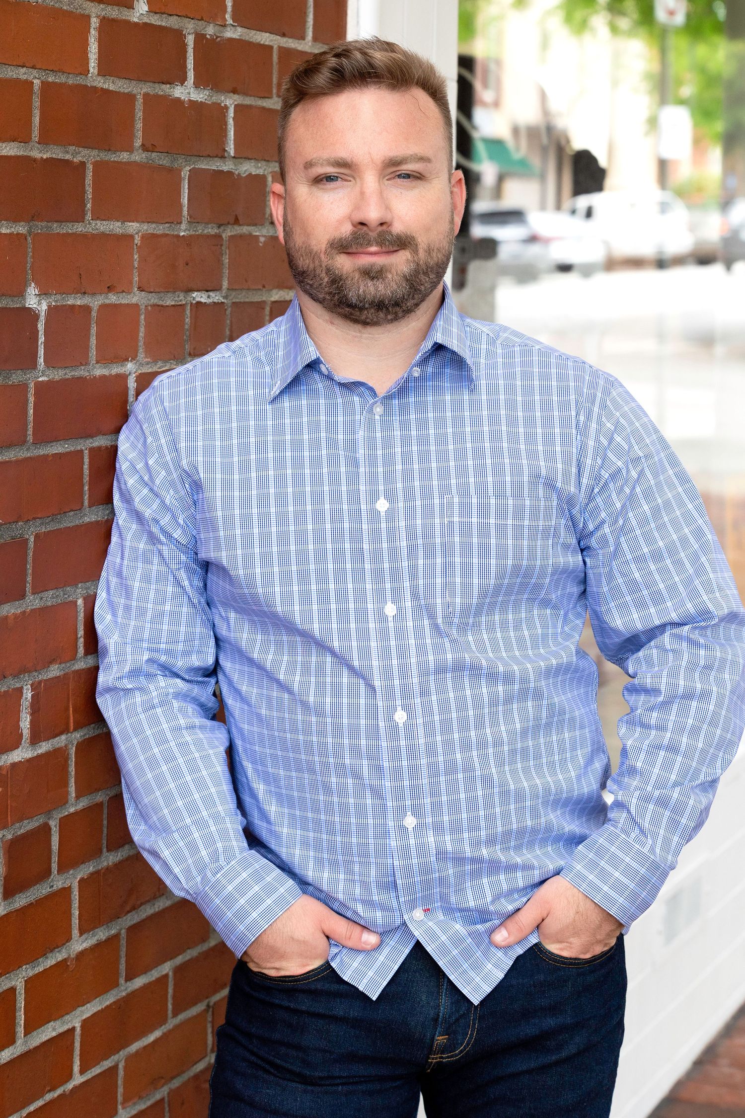 Professional headshots of person in blue checkered shirt against brick wall backdrop.