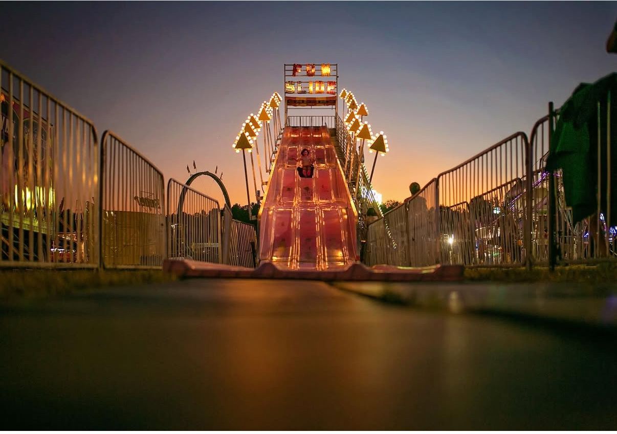 Silhouetted carnival rides and attractions at dusk create a magical fairground atmosphere.