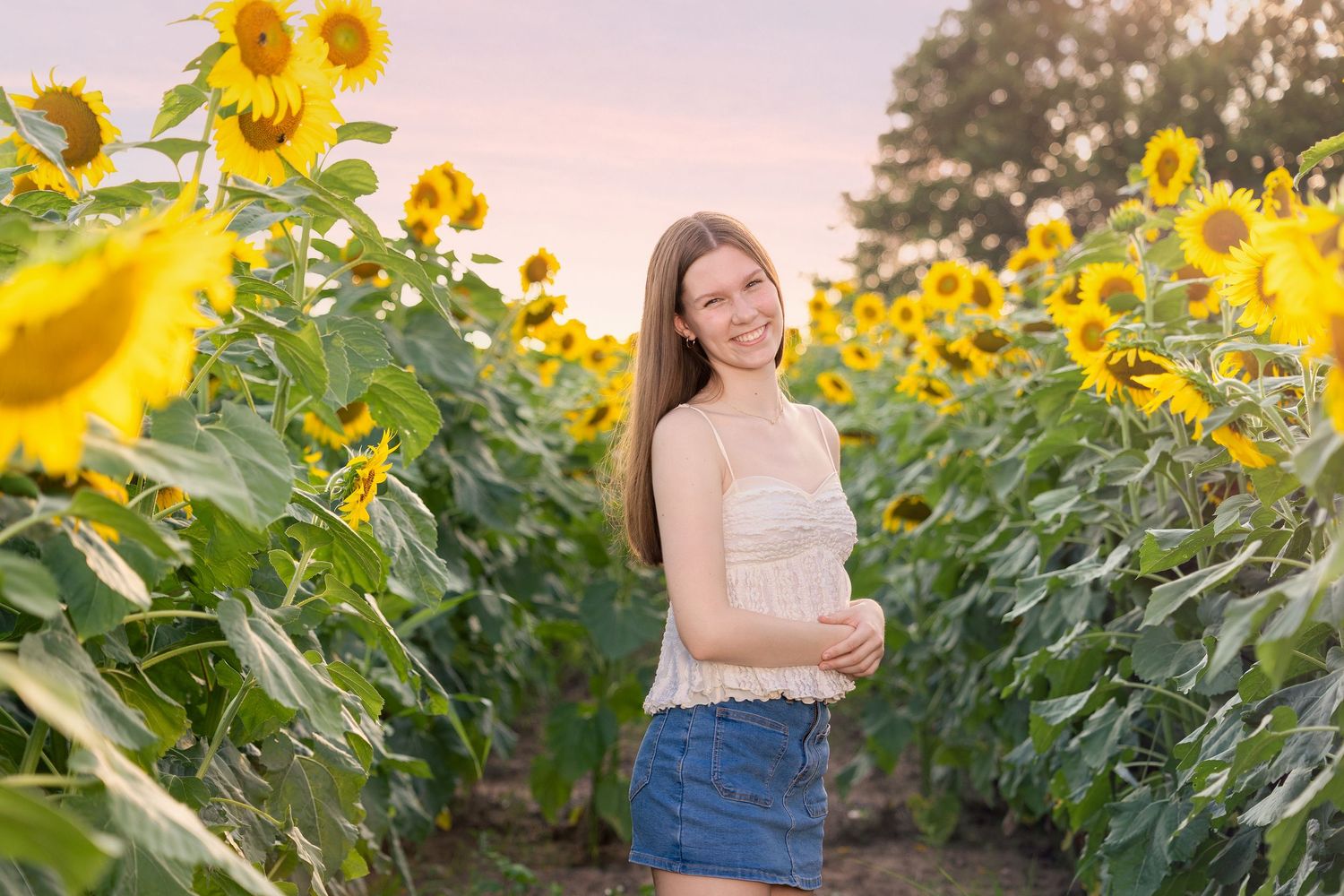 Someone poses in a vibrant sunflower field during golden hour as warm sunlight filters through the tall yellow blooms.