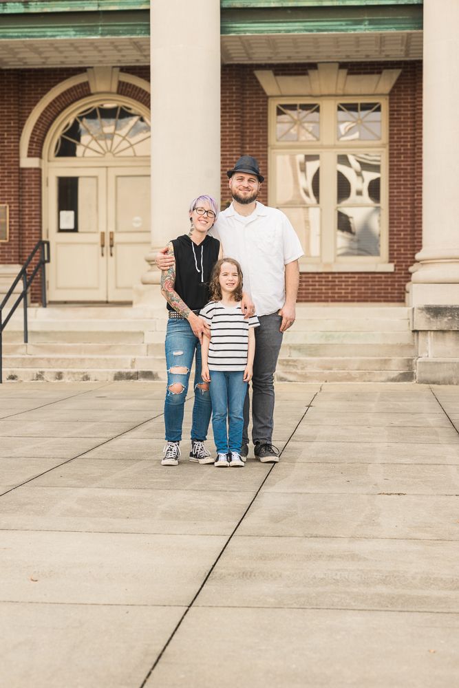 Family sitting on stone steps outside historic brick building with arched windows.