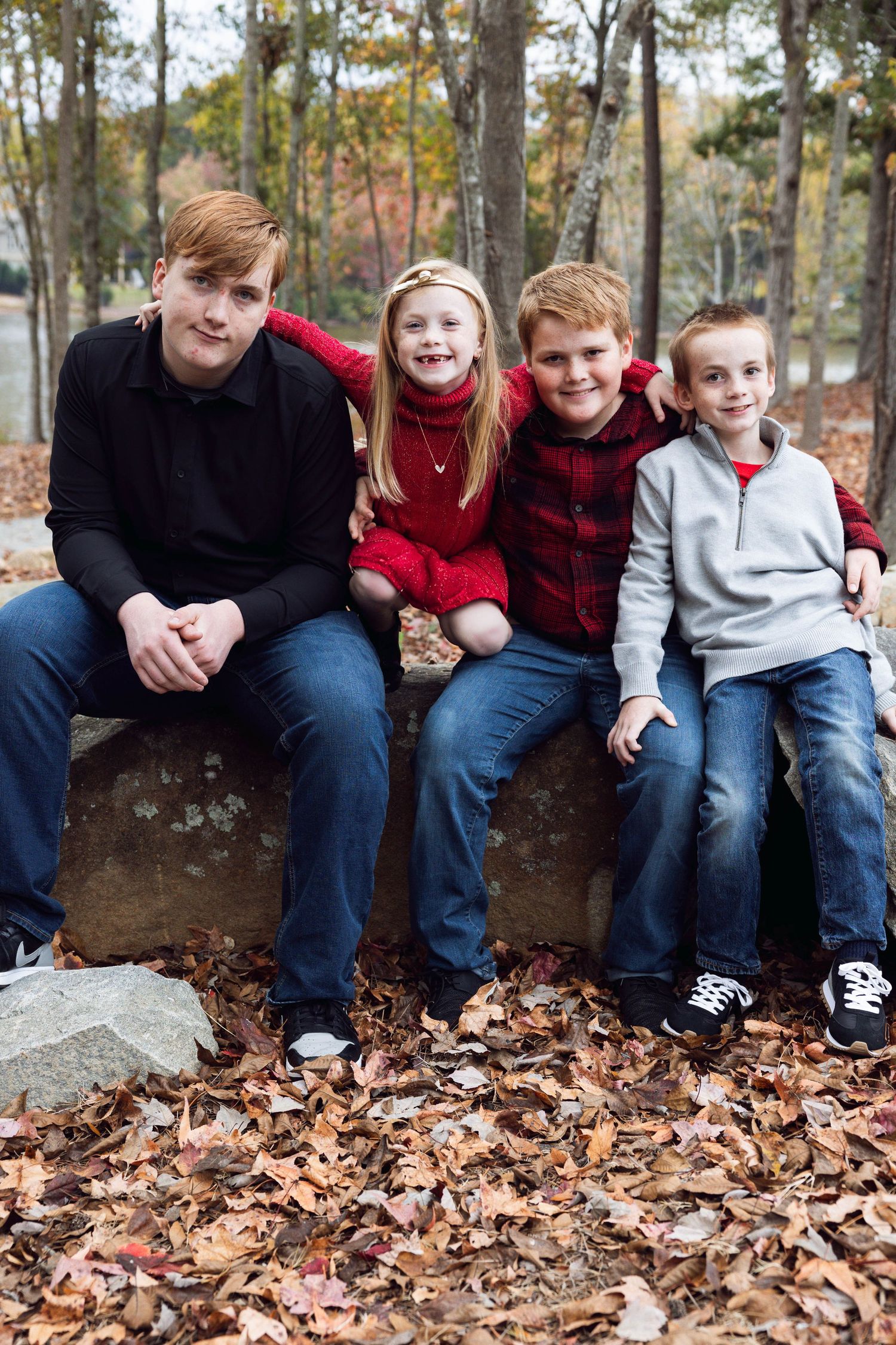 Family seated on rock wall among fallen autumn leaves.