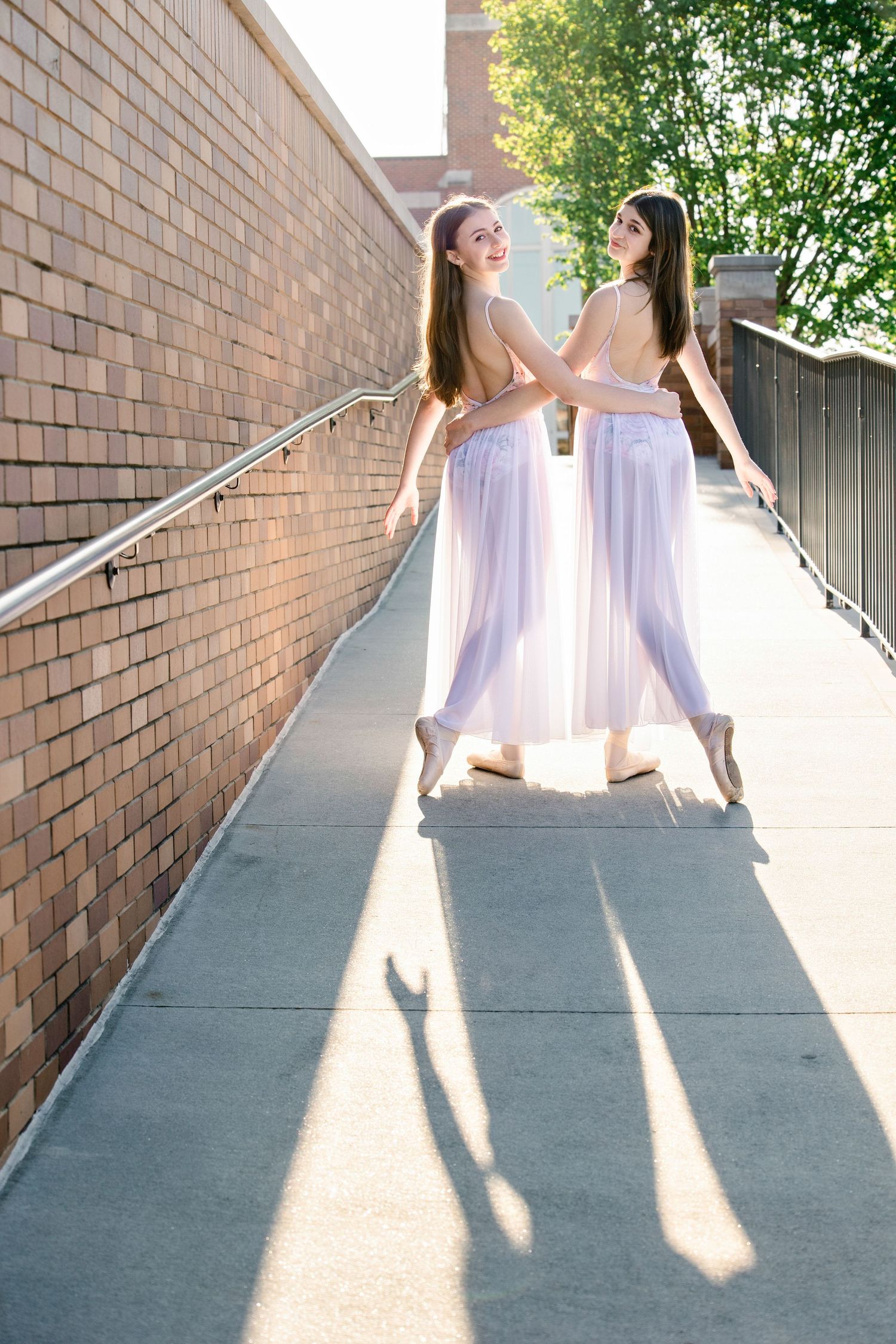 Dancers in white dresses create dramatic shadows while performing along a concrete walkway.