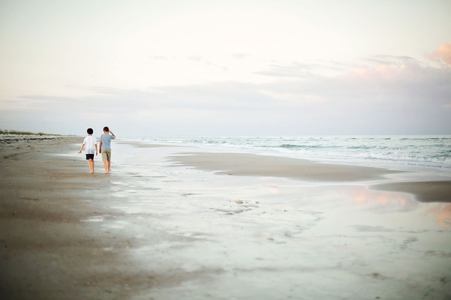 Silhouettes of people walking along a misty beach at sunset with ocean waves in the background.