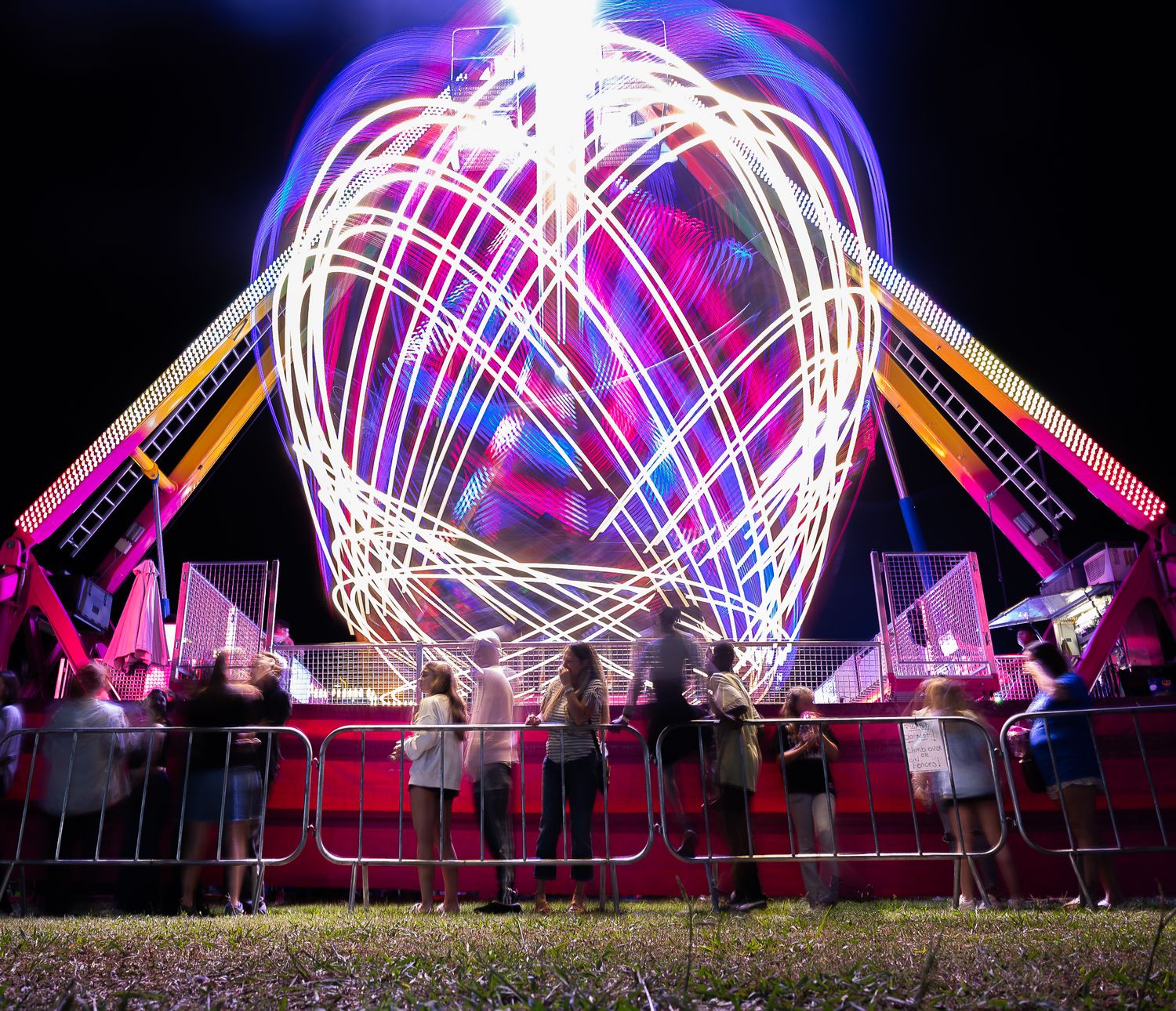Long exposure shot of carnival ride creating glowing white light trails in circular pattern at night.