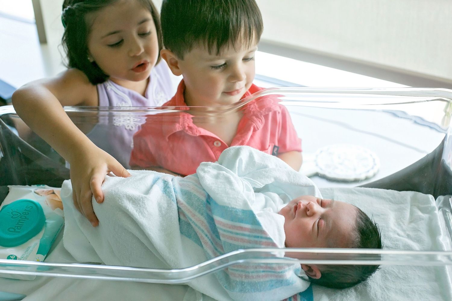 Young children peering into a hospital nursery window at a newborn baby.