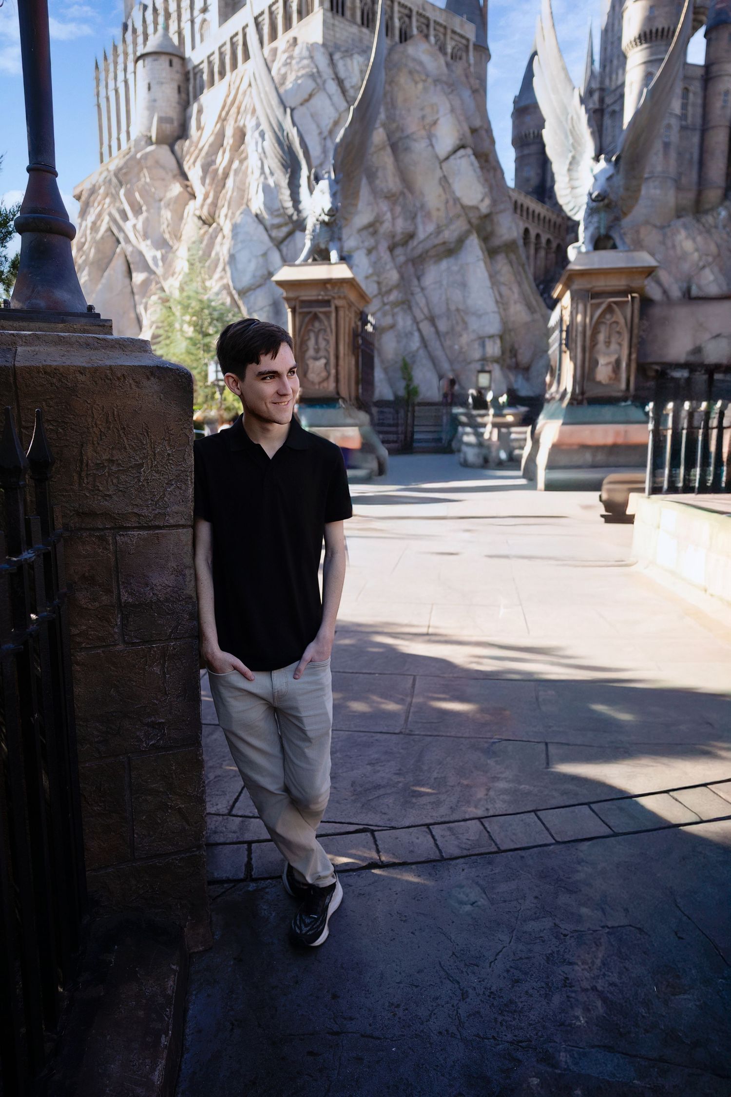 Young man in black polo and khaki pants poses at Wizarding World of Harry Potter theme park.