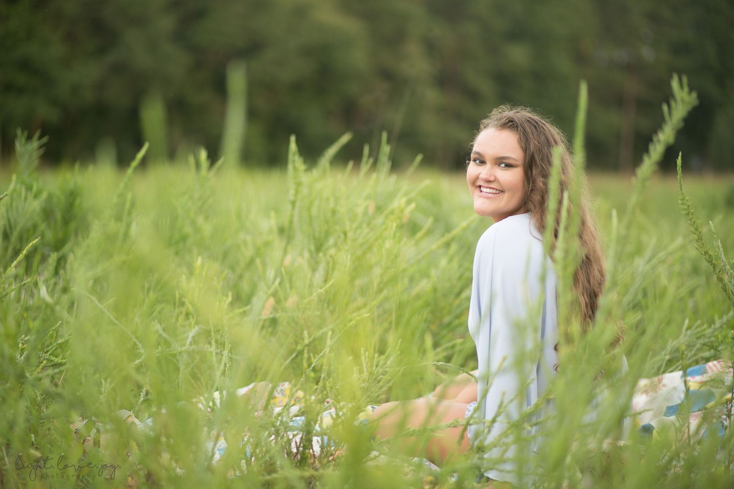 A couple poses together in a sunny field of tall grass and wildflowers during a romantic outdoor photoshoot.