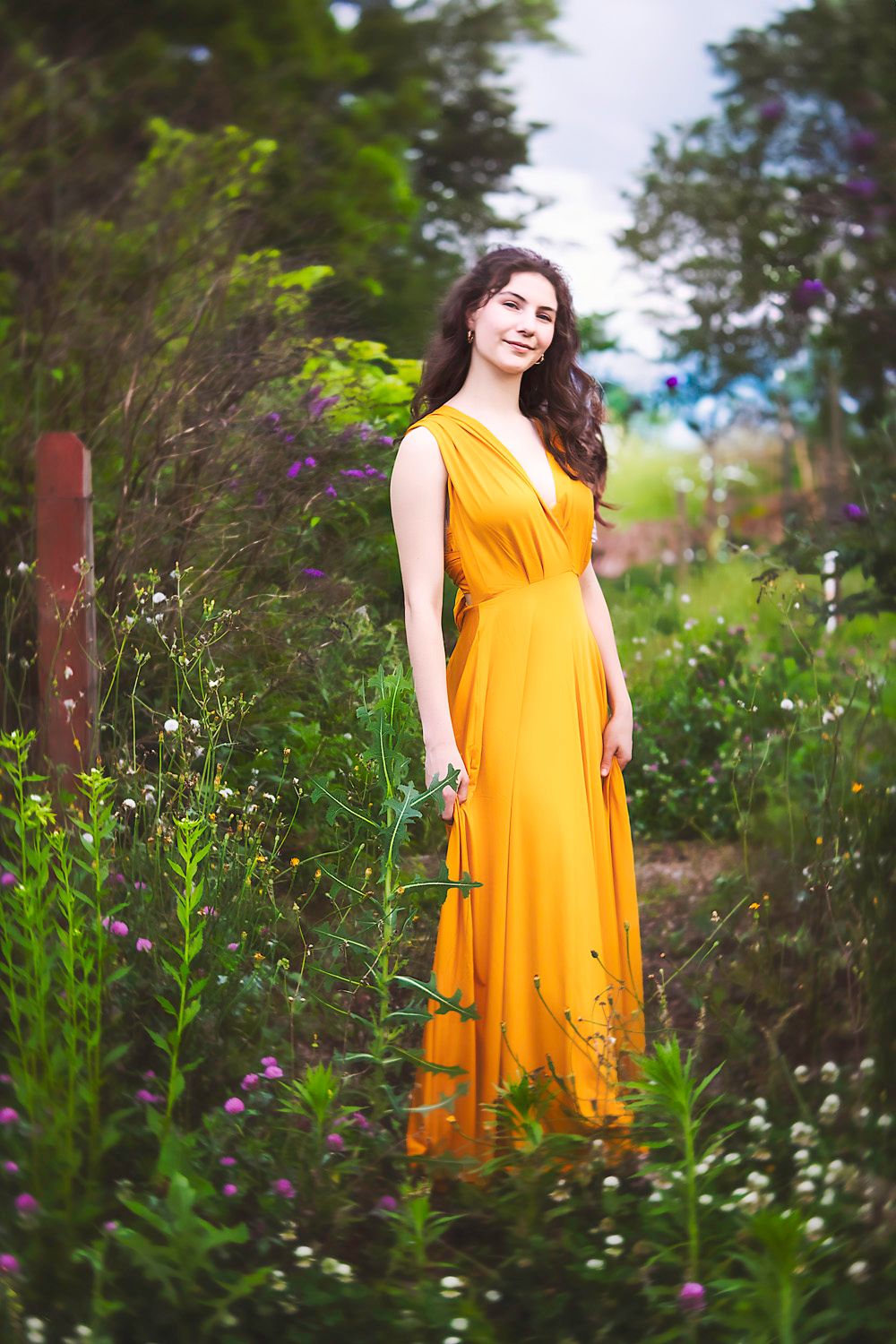 Yellow dress contrasts beautifully with lush green garden foliage in outdoor portrait session.