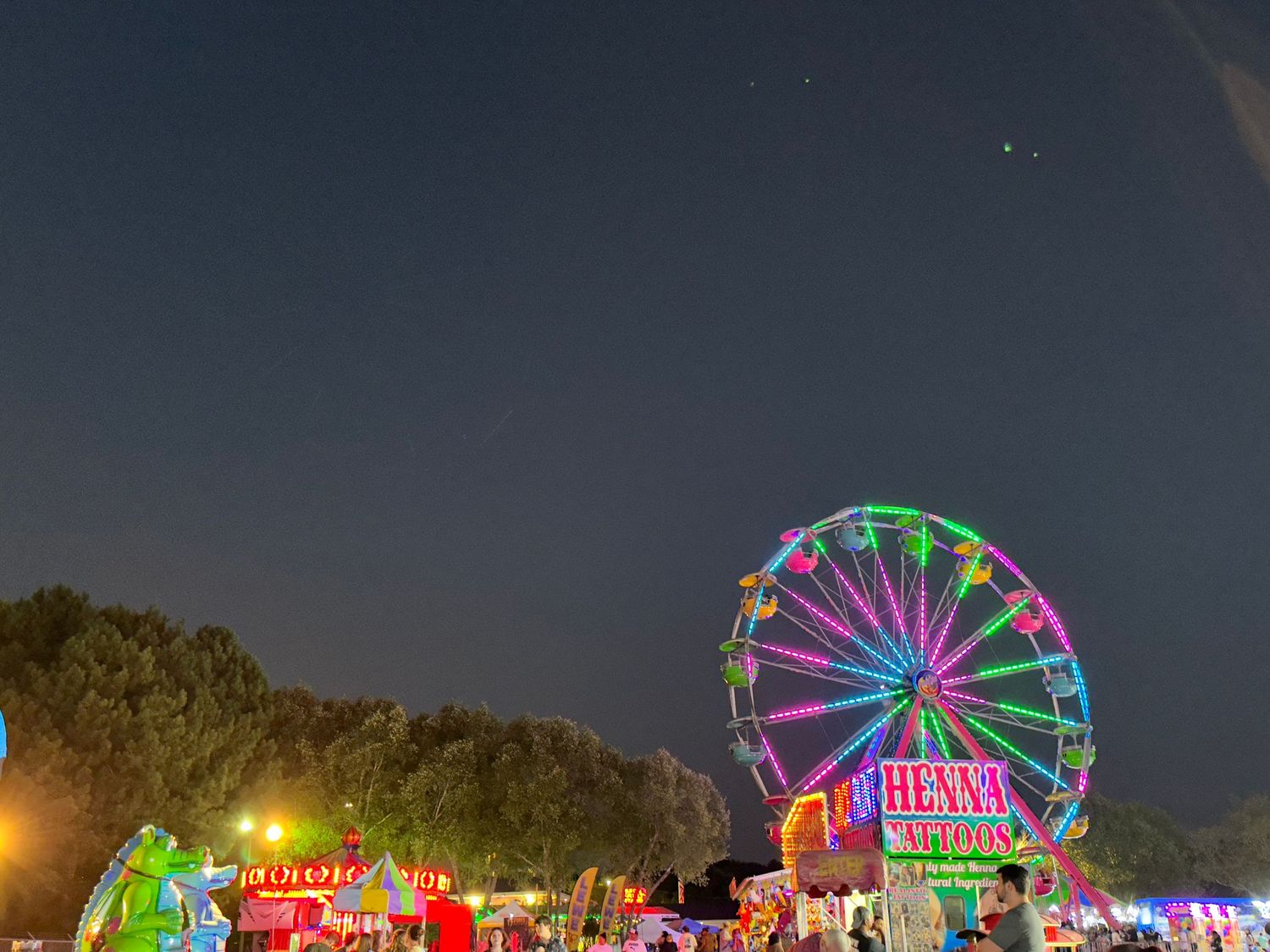 Colorful Ferris wheel and carnival rides illuminated against dark night sky.