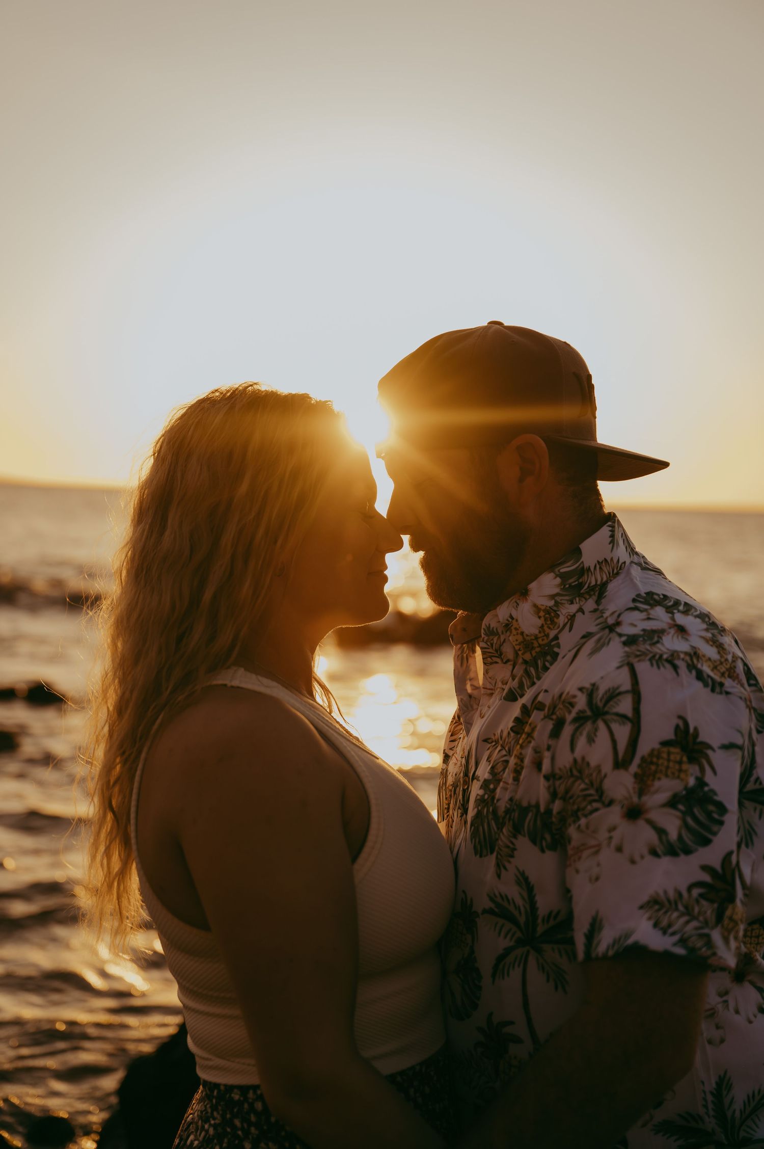 A couple shares an intimate moment at sunset by the ocean, silhouetted against the golden light.