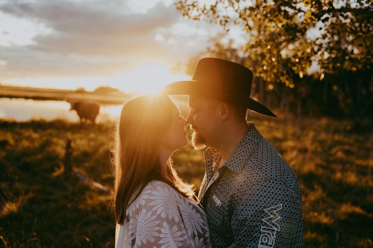 Couple embraces during golden sunset in nature with sunlight streaming through trees.