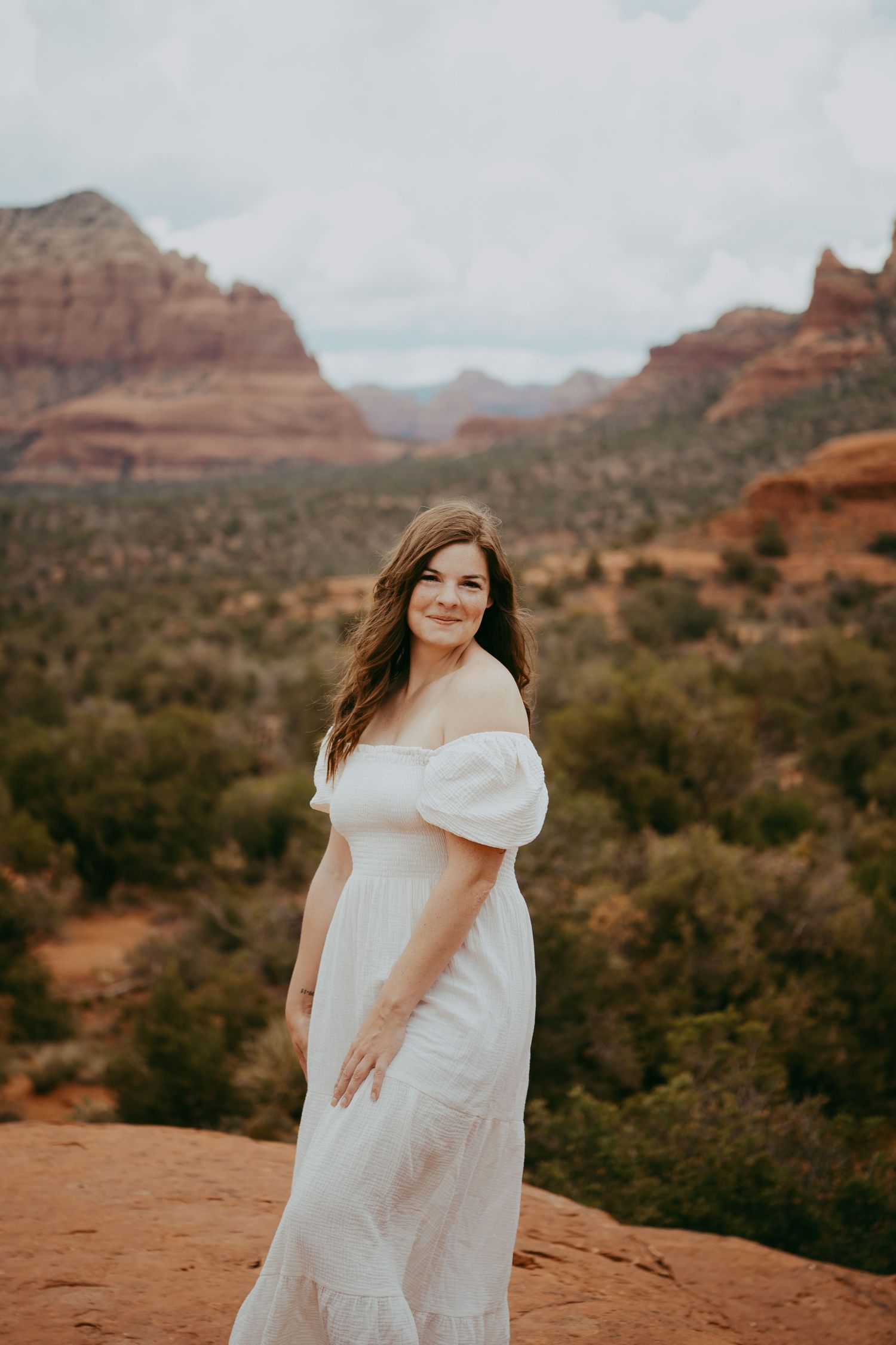 A person in a white dress twirls against the stunning red rock formations of Sedona's desert landscape at sunset.