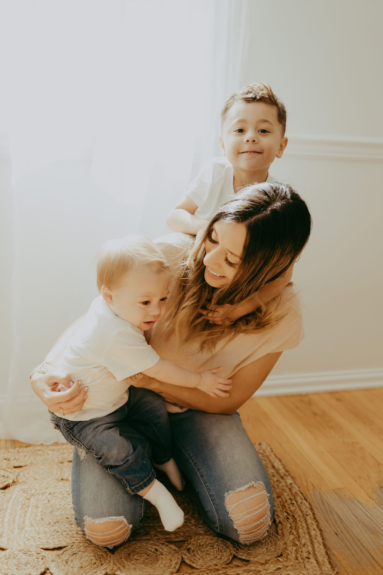 A parent and child share tender moments playing together on a woven rug in a bright, minimalist room.