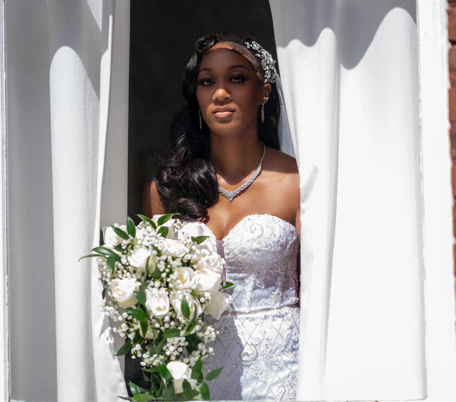 Beautiful natural light covers the skin of the bride looking out of her window, captured by the best wedding photographers in Florida.