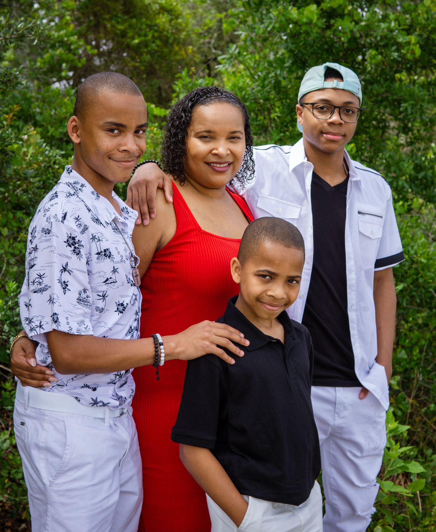 A joyful family poses outdoors among lush green foliage, wearing stylish outfits in a warm portrait.