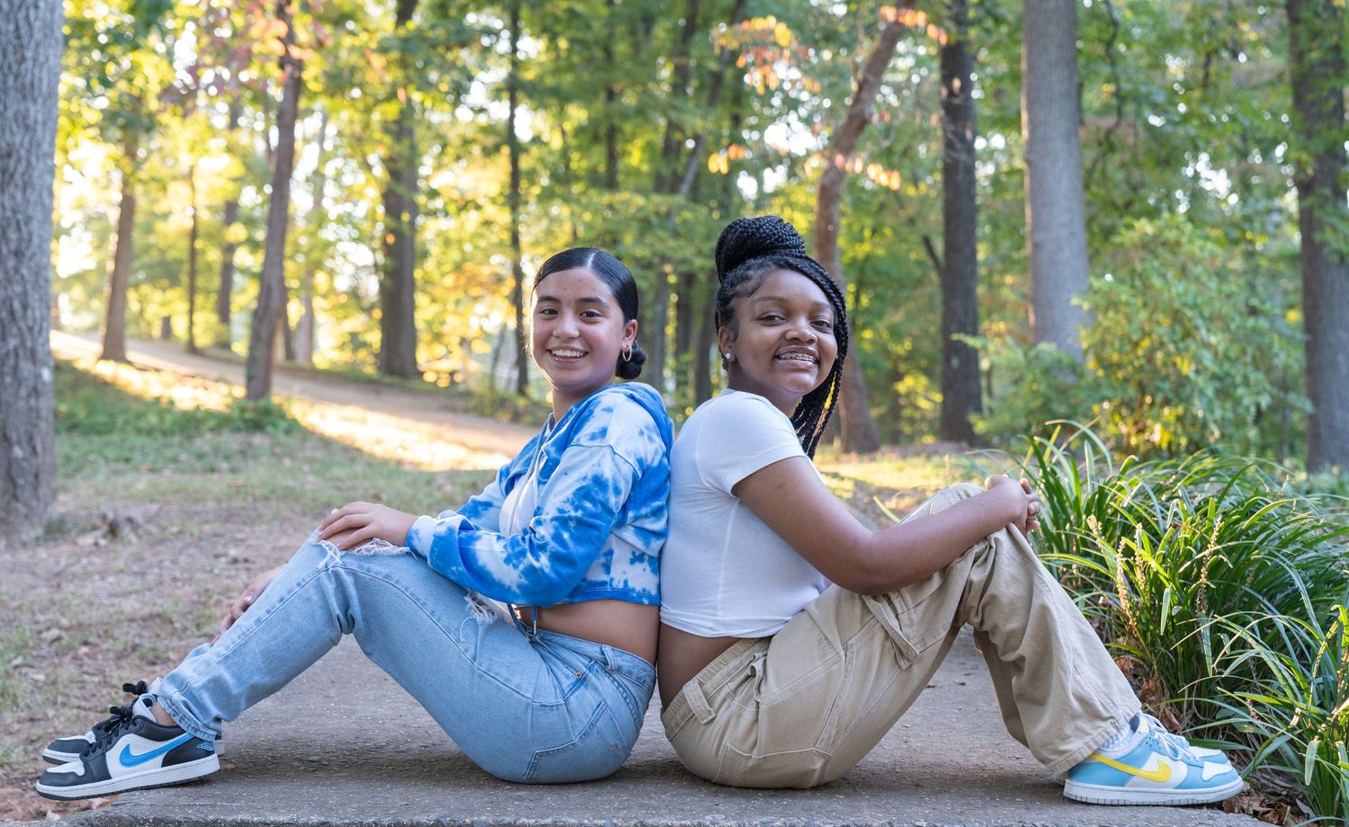 Two best friends sitting back-to-back on a path in a park.