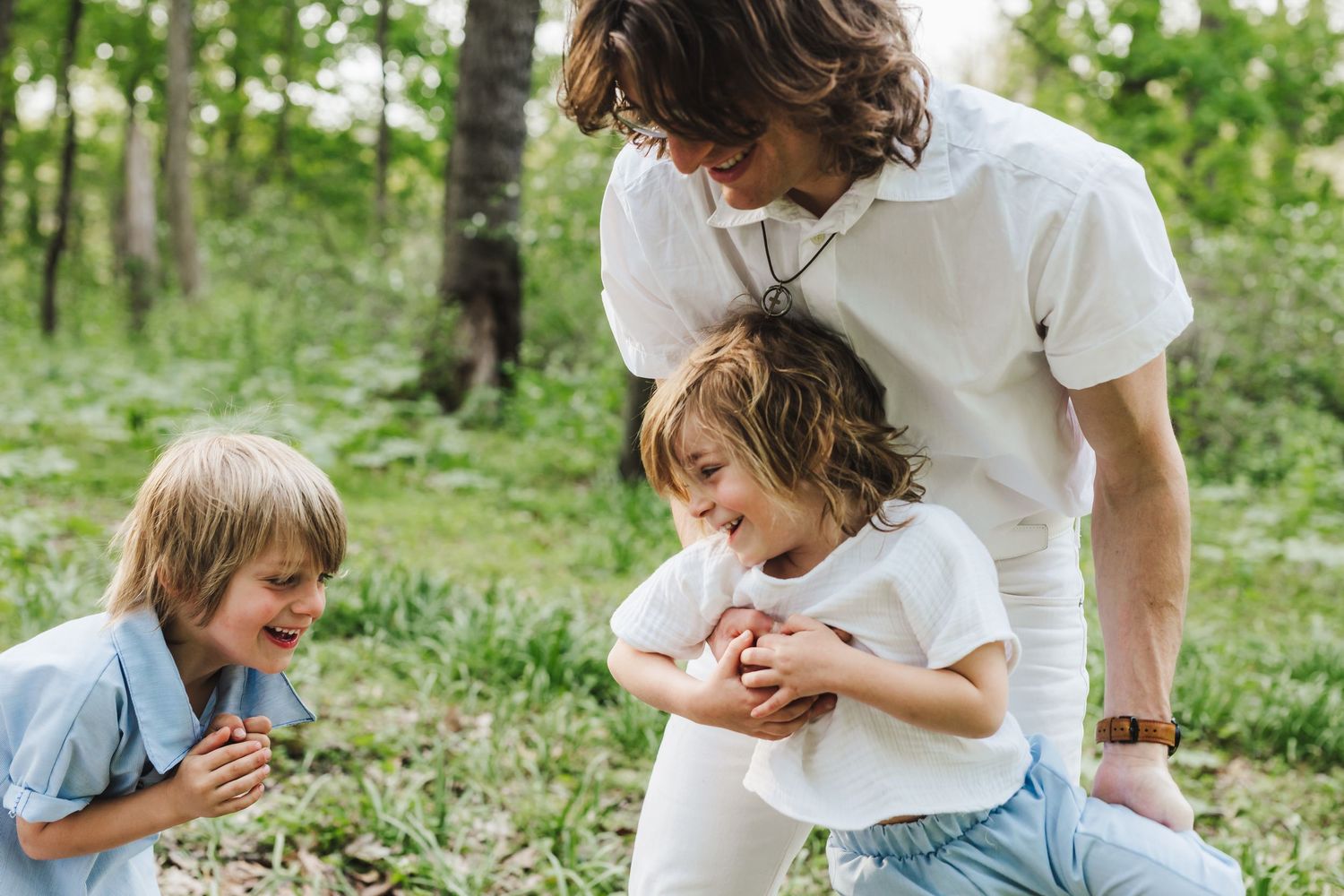 Group playing and laughing together outdoors in a green forest setting on a sunny day.