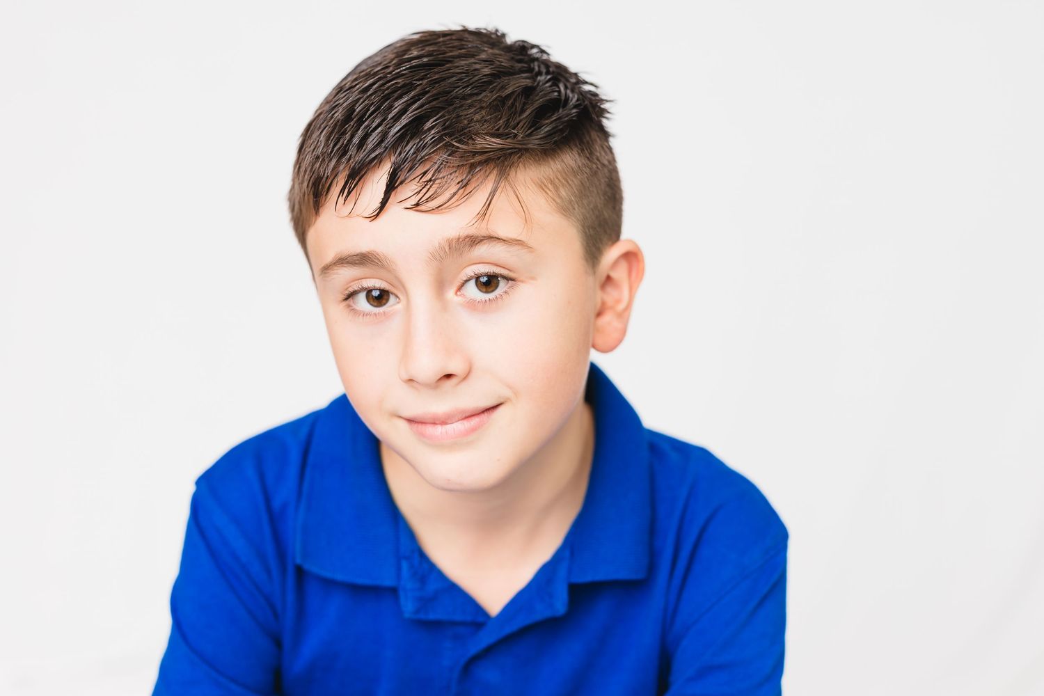 Child in bright blue polo shirt poses against white background with friendly expression.