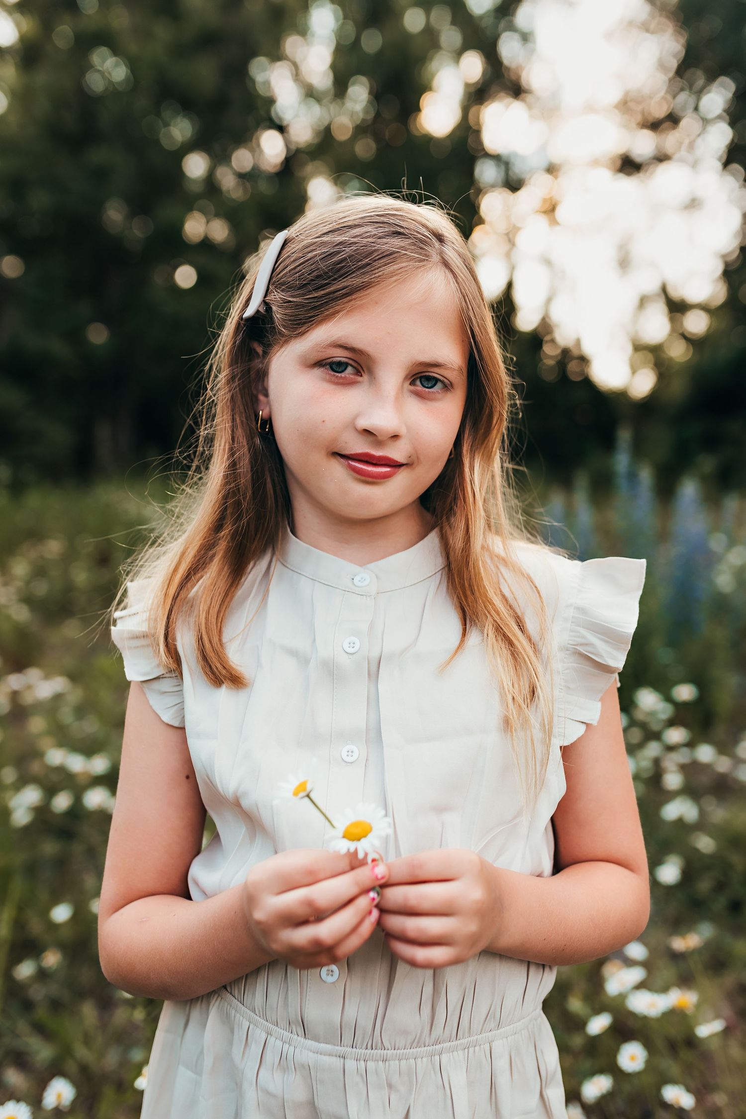 Young girl in white dress holding wildflowers in summer garden at sunset.