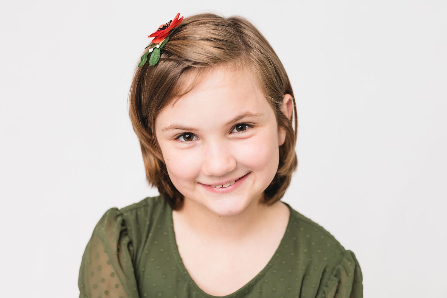 A person cheerfully poses against a white background wearing a green top with red and holly berry holiday accents.