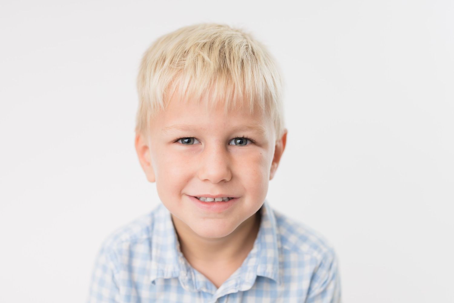 Three headshots of a young child with blonde hair wearing a light blue checkered shirt against a white background.