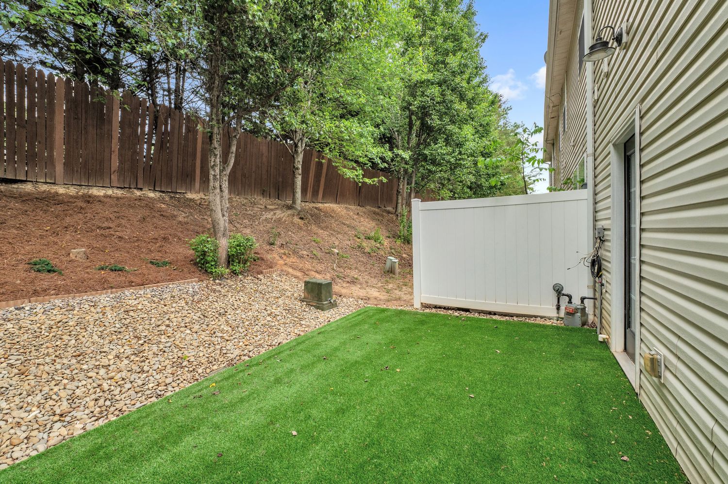 Backyard space with artificial turf, gravel border, and wooden privacy fence.