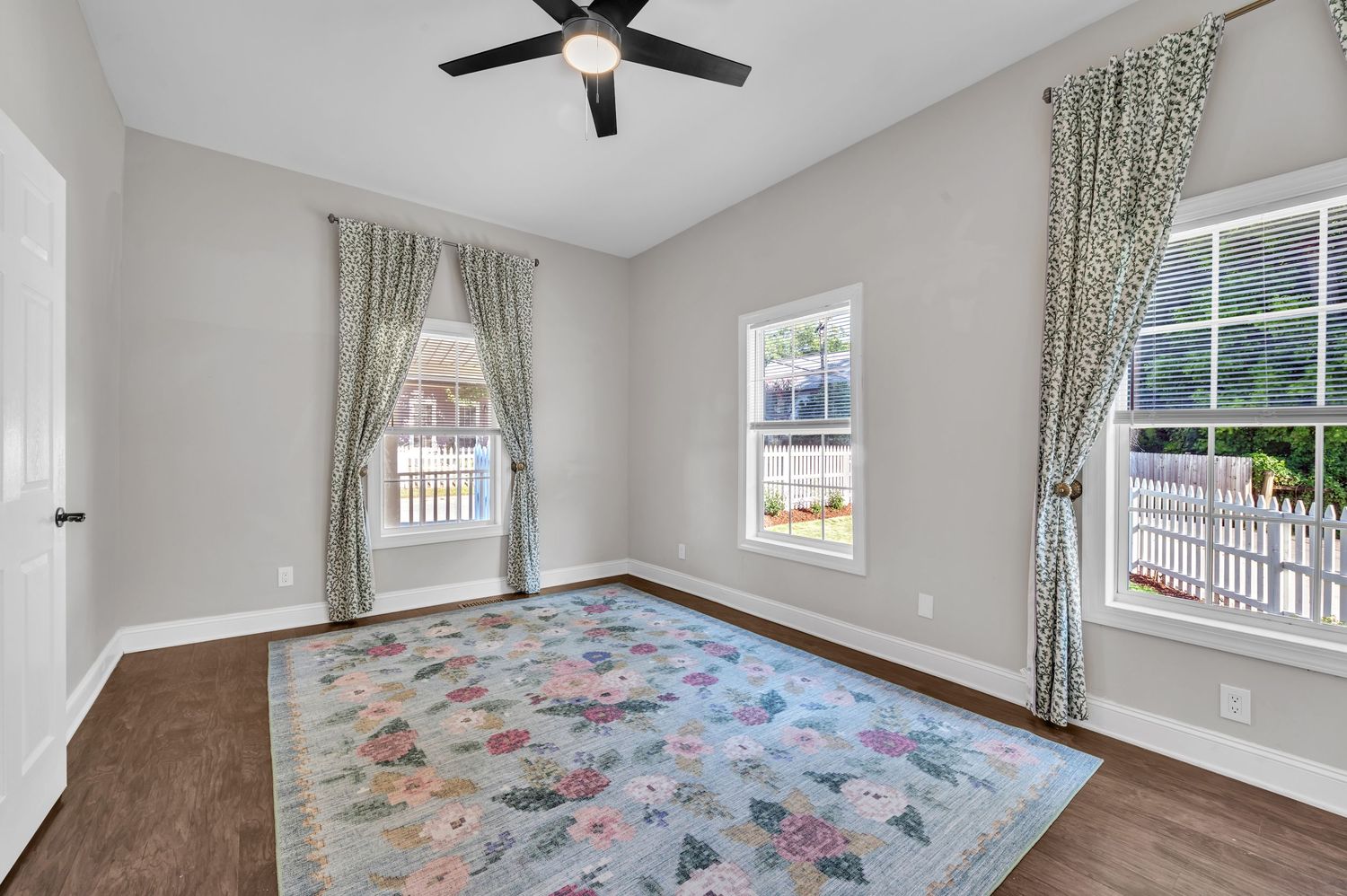 Spacious room with hardwood floors, floral area rug, and patterned curtains by windows.