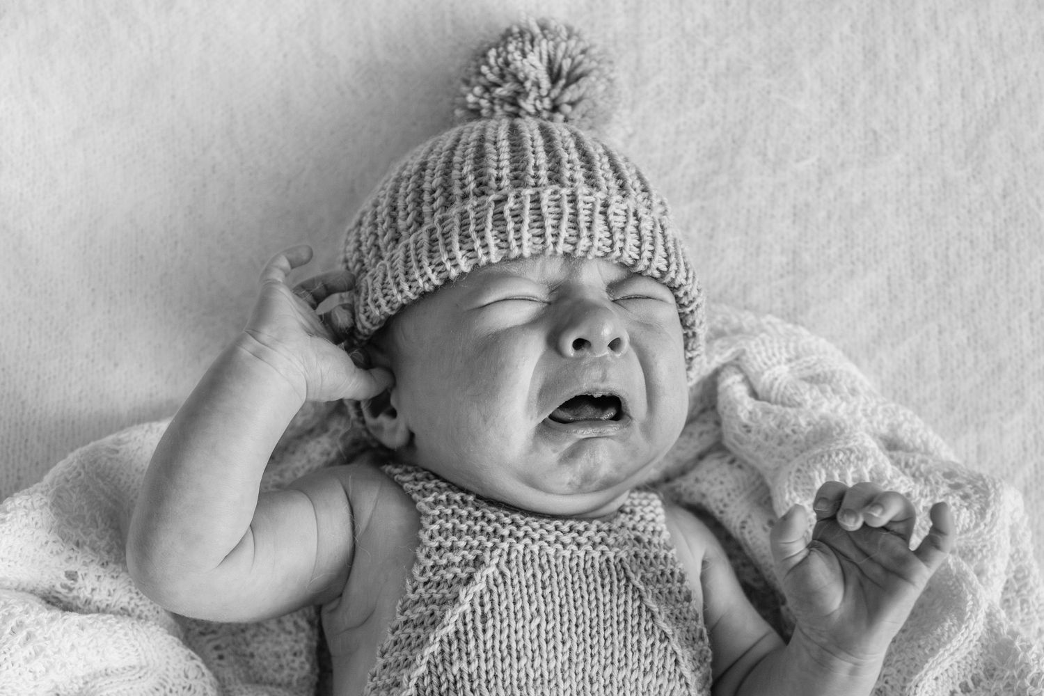 Baby wearing a knit hat laying on white blanket in black and white photography.