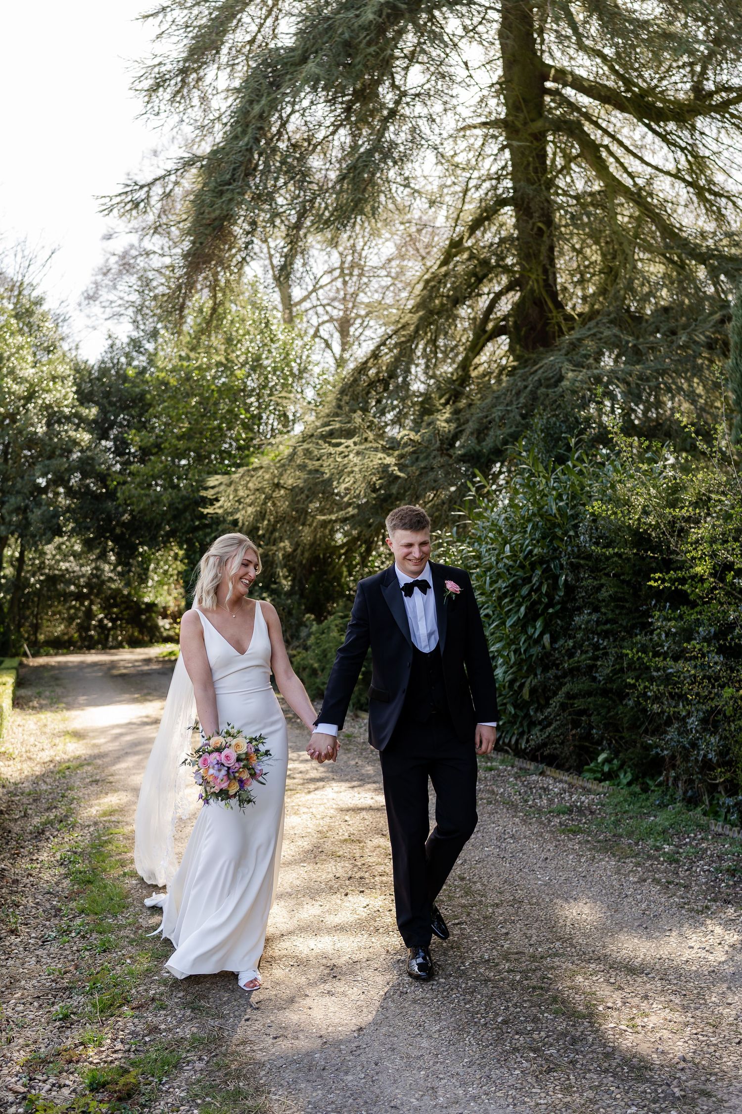 Lovely couple walking through the trees at luxury wedding venue Wootton Hall in Lincolnshire. Colourful florals.