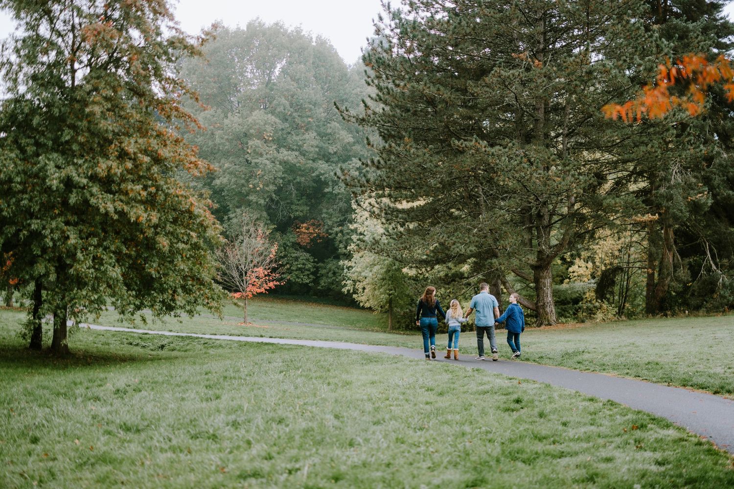 Three people walk along a curved path through a scenic park with autumn trees.