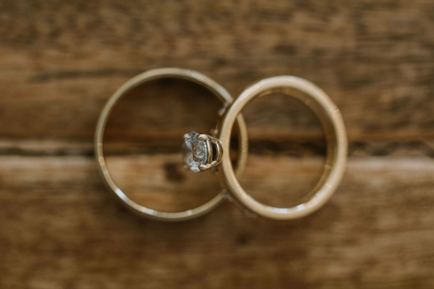 Two wedding rings photographed in macro detail showing diamond engagement ring and band on wooden surface.