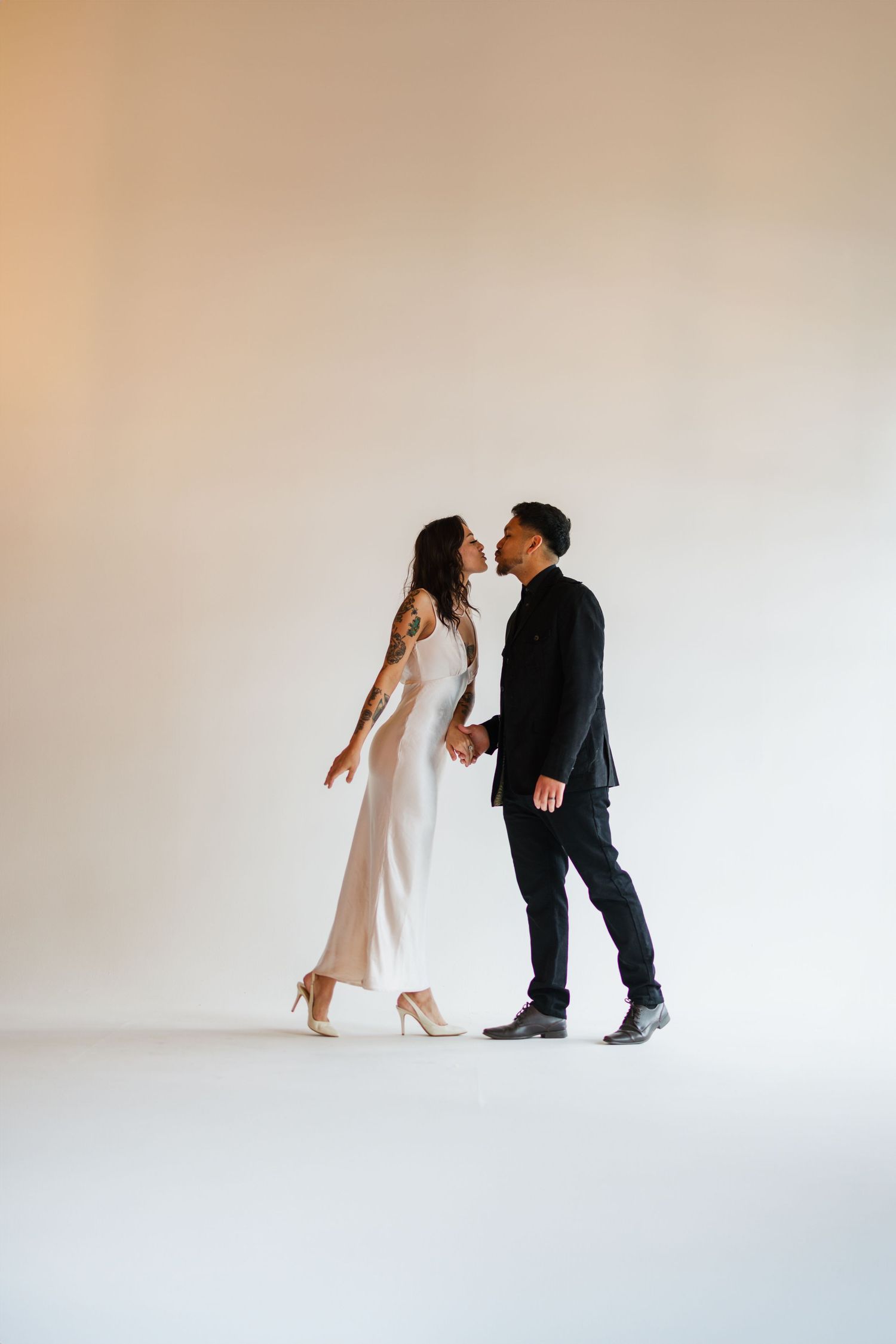 A couple in elegant attire sharing a romantic moment, woman in white gown and man in black suit holding hands.