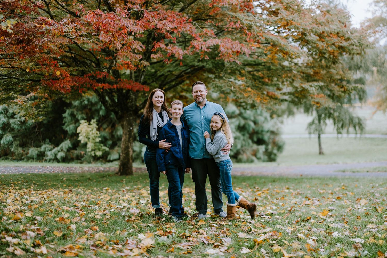 A family poses together under vibrant fall foliage in a park setting.