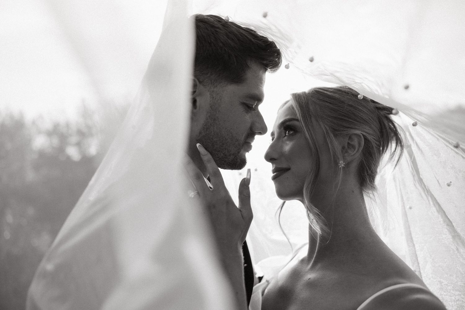 Black and white wedding photo of bride and groom sharing intimate moment under veil.
