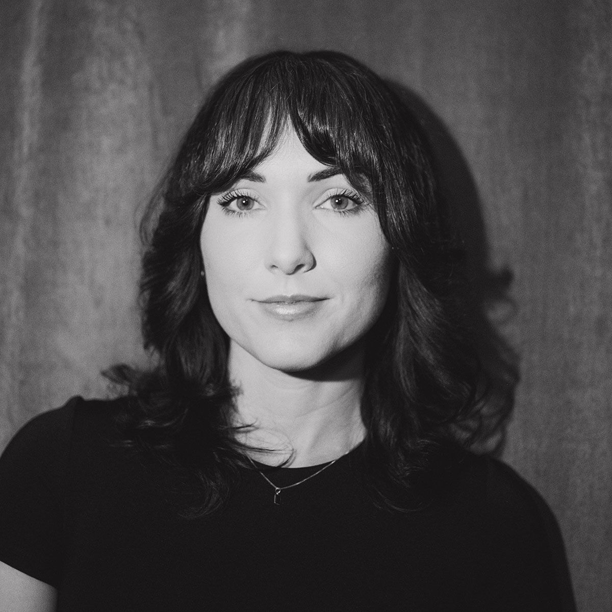 Black and white portrait of a woman with bangs and wavy hair wearing a black top.