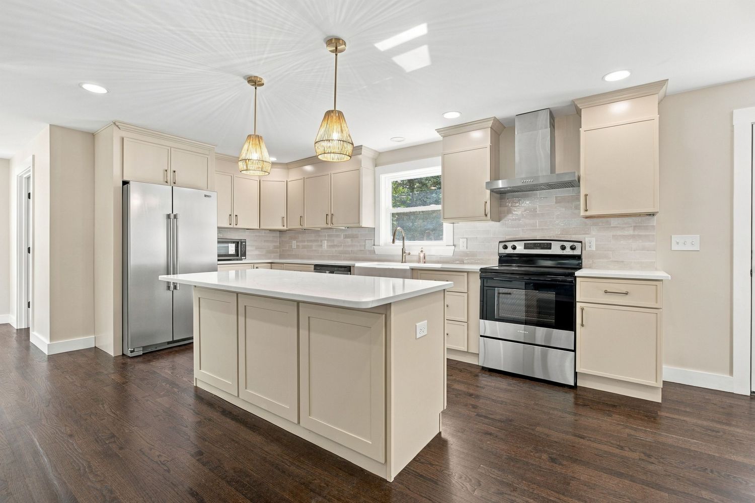 Modern kitchen with cream cabinets, stainless steel appliances, center island, pendant lights, and dark hardwood floors.